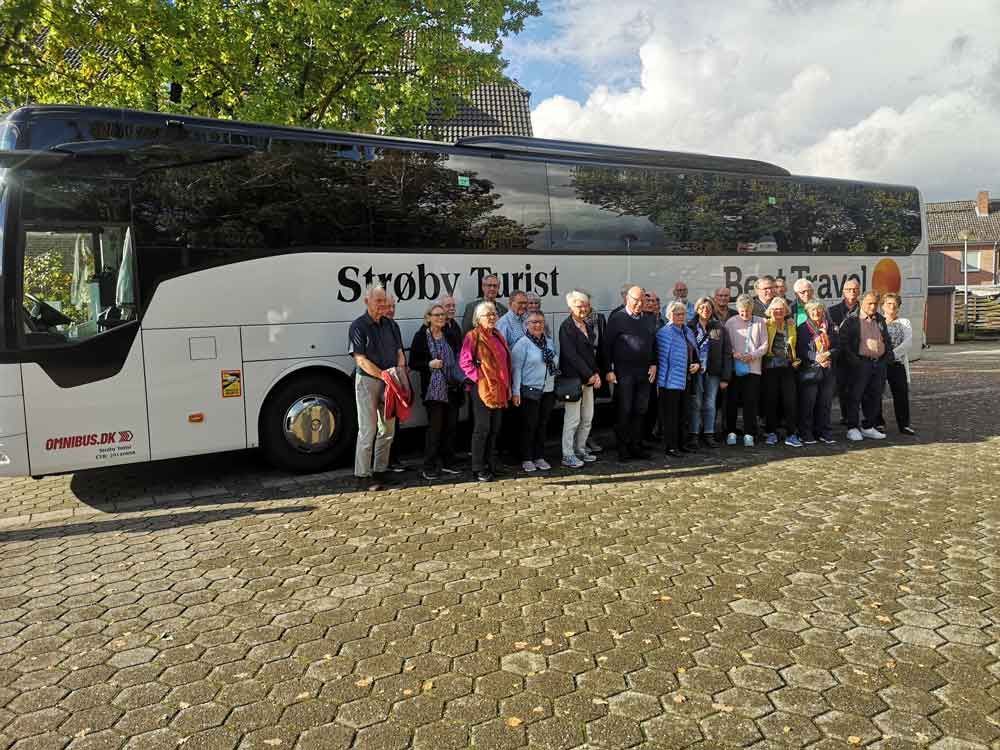 Gruppe af seniorer står ved siden af ​​en hvid turistbus mærket 