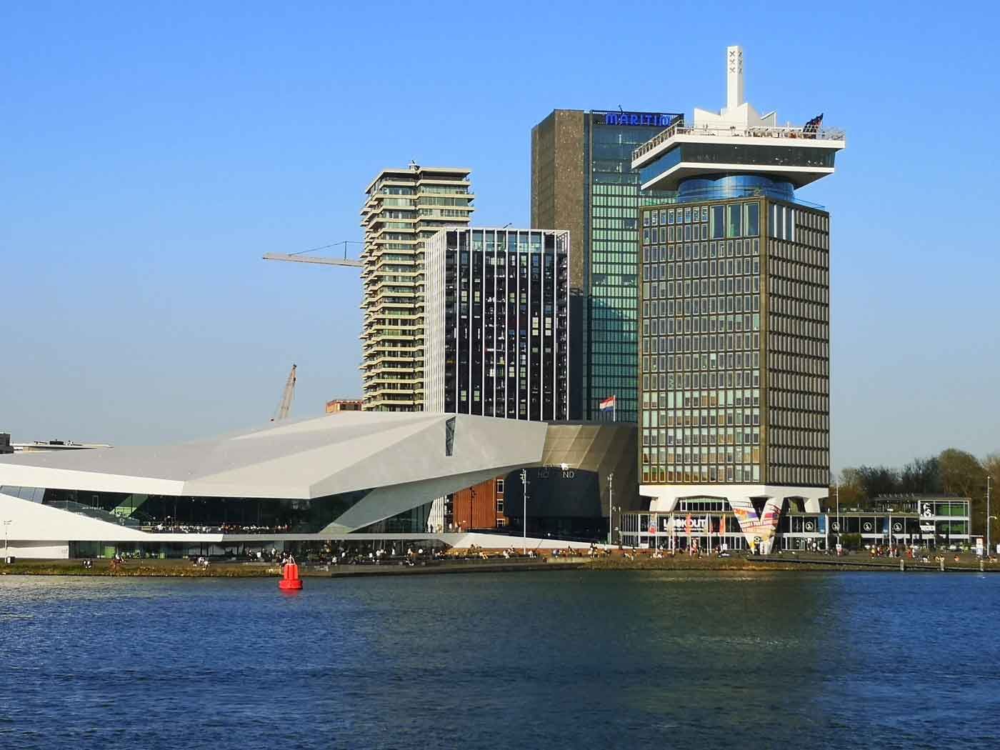 Amsterdams skyline: moderne bygninger langs havnefronten, herunder en hvid, kantet bygning og en høj skyskraber.