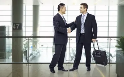 Two men in suits are shaking hands in an airport.