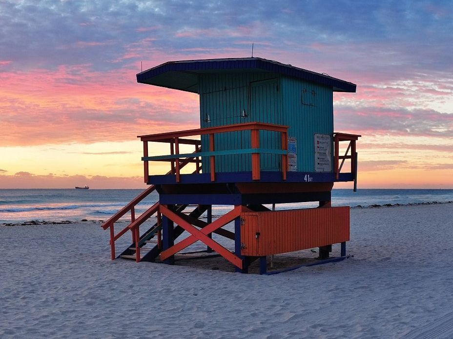 A Miami Beach bridge over a body of water with a city skyline in the background at sunset.