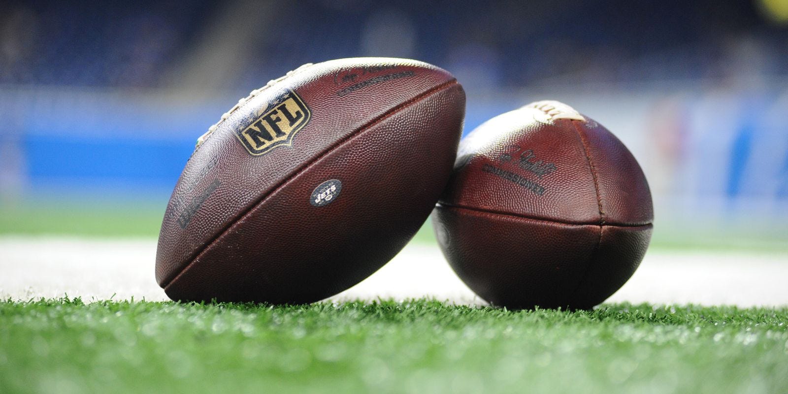 Two nfl footballs are sitting on top of a football field.