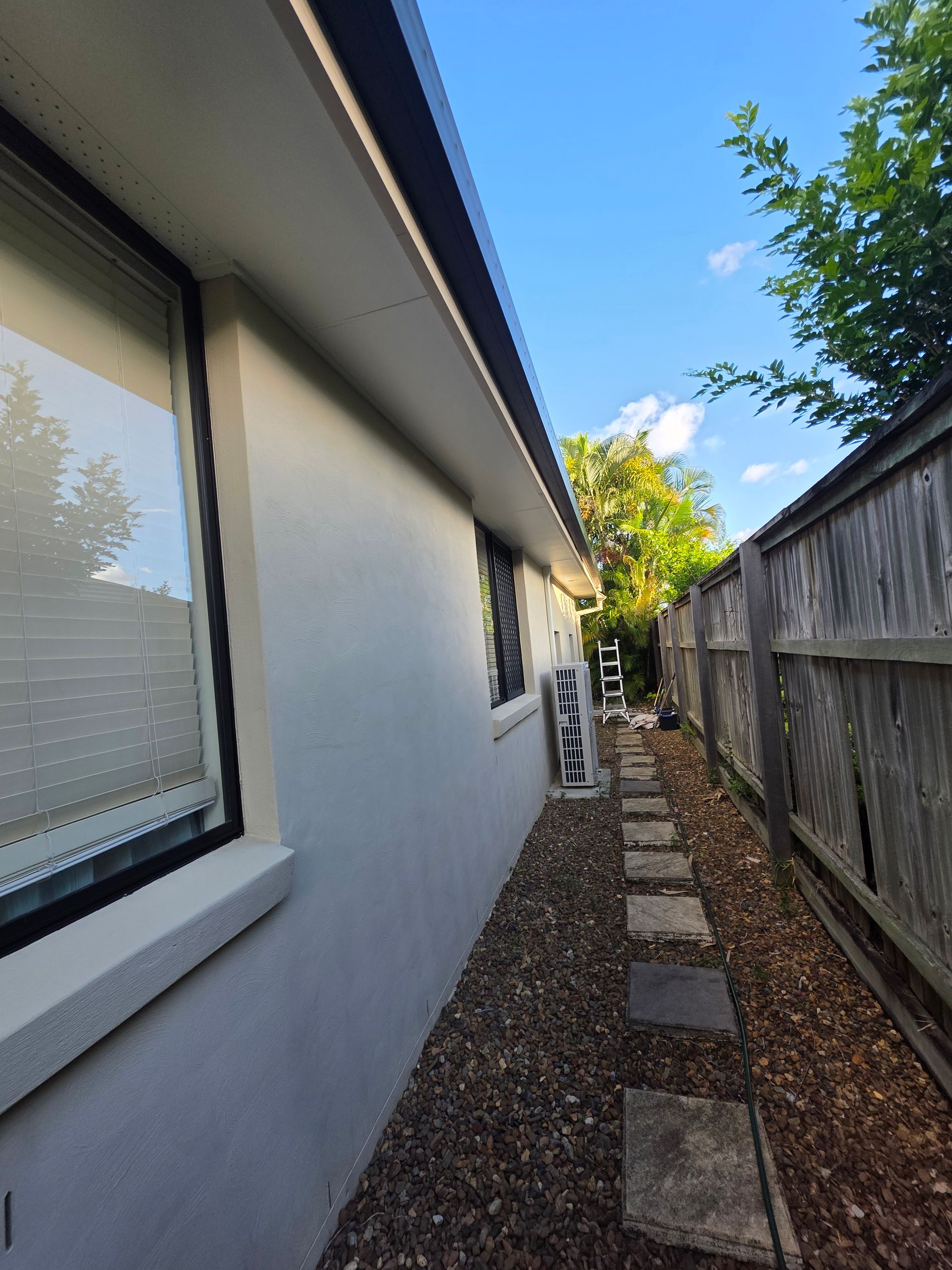 Side view of a house with a window, pathway, and wooden fence on the right side.