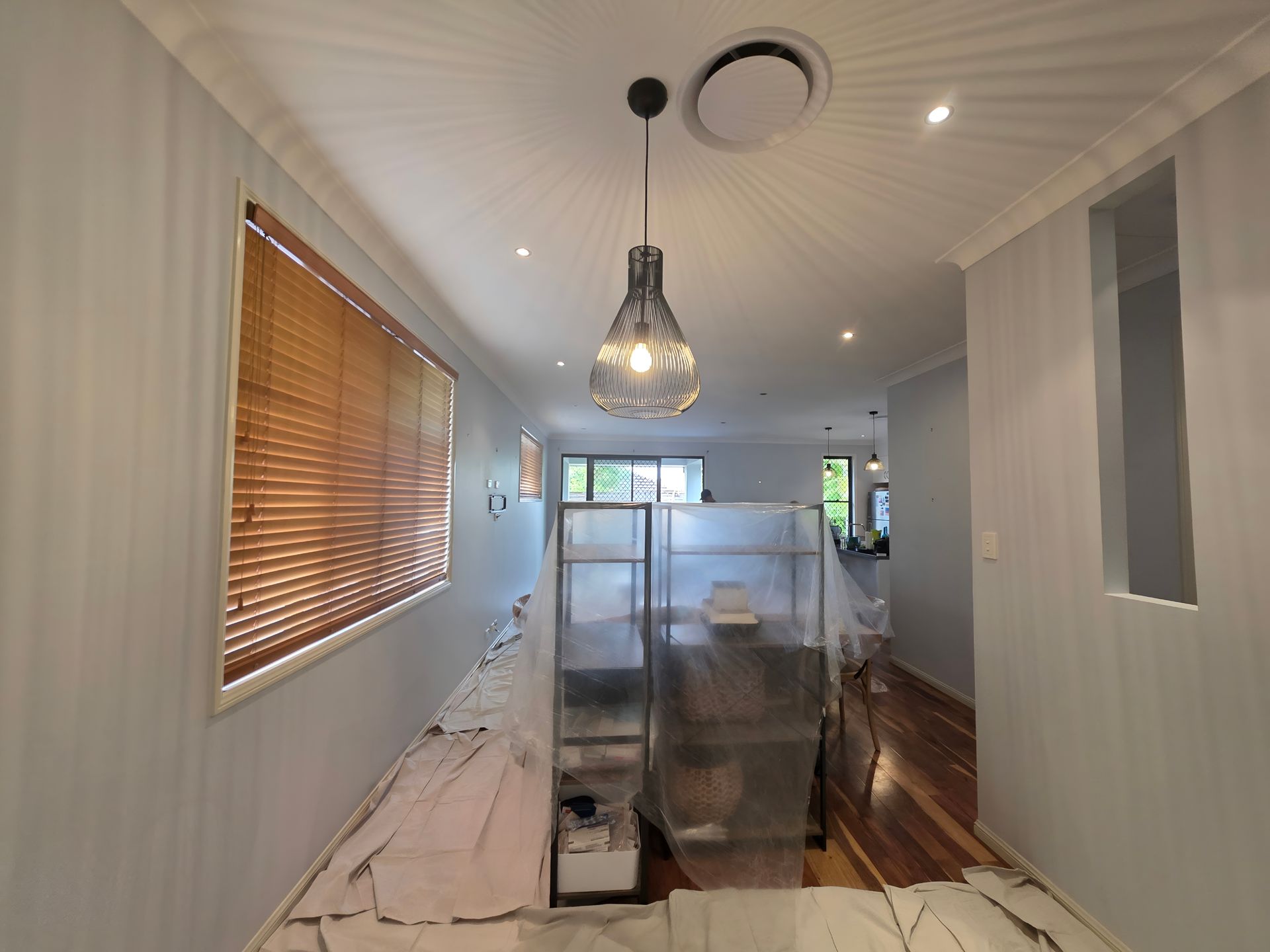 Narrow hallway with wood blinds, a pendant light, and a covered shelving unit.