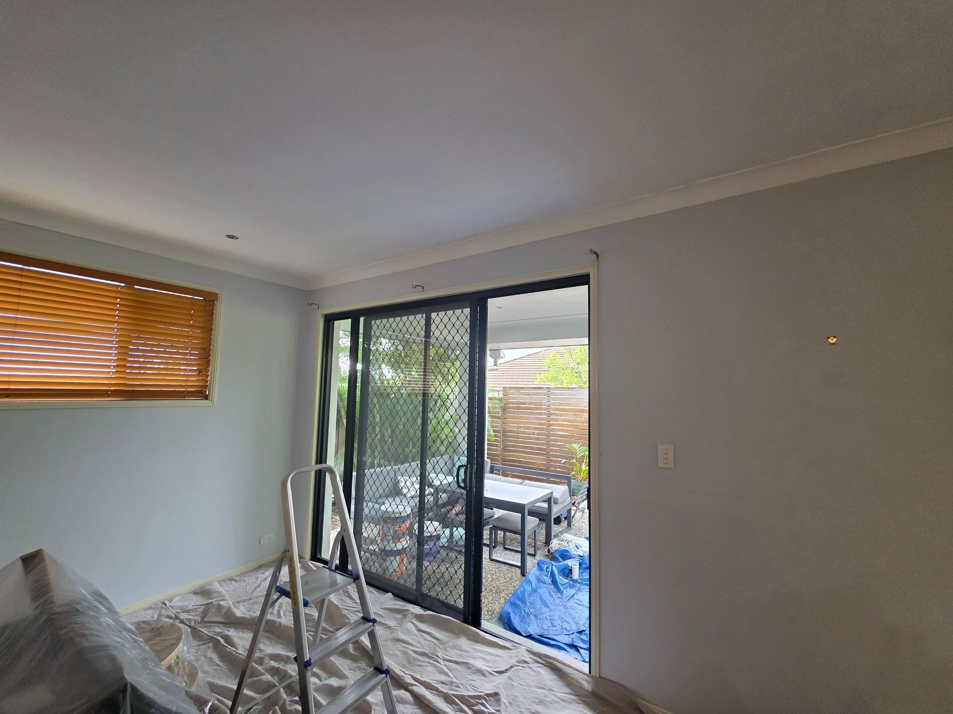 Interior room with light blue walls, sliding glass door to a patio, and a ladder on drop cloths.