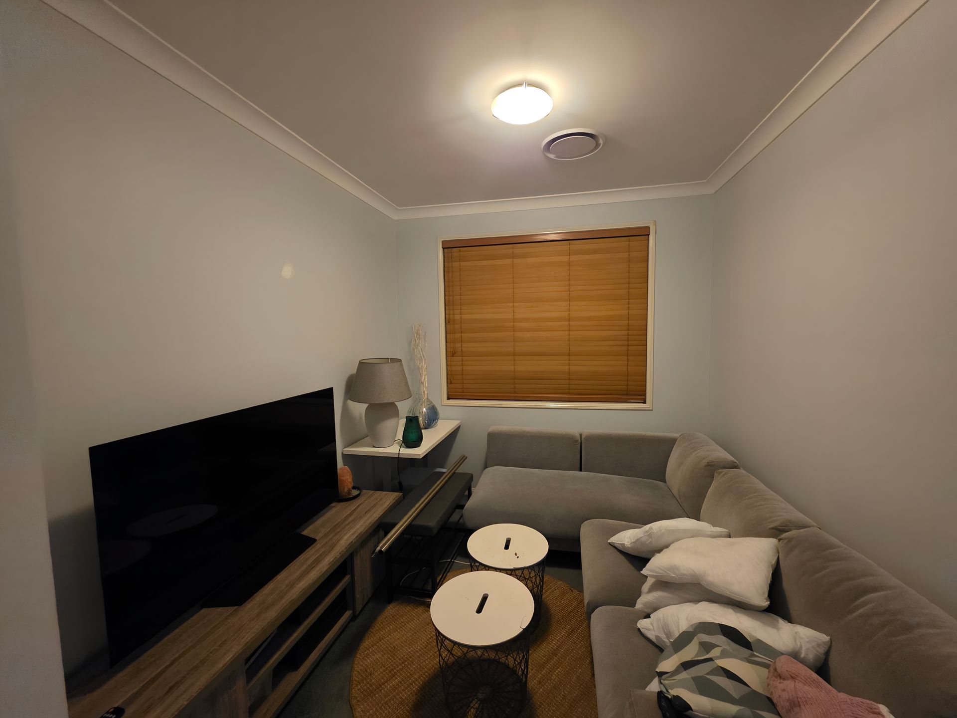 Living room with gray sectional sofa, TV, wooden blinds, and two round coffee tables.