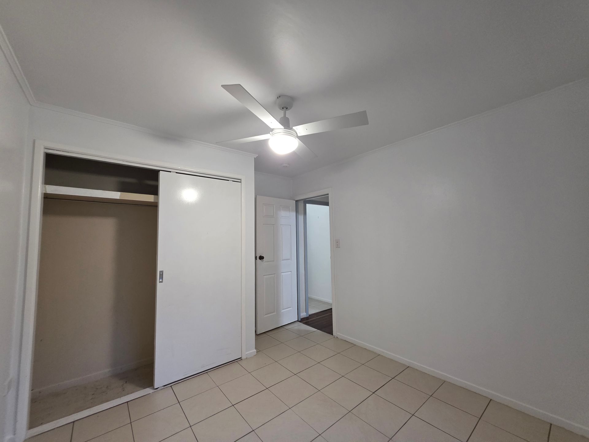 Empty bedroom with closet, white walls, and a ceiling fan. Tile floor.