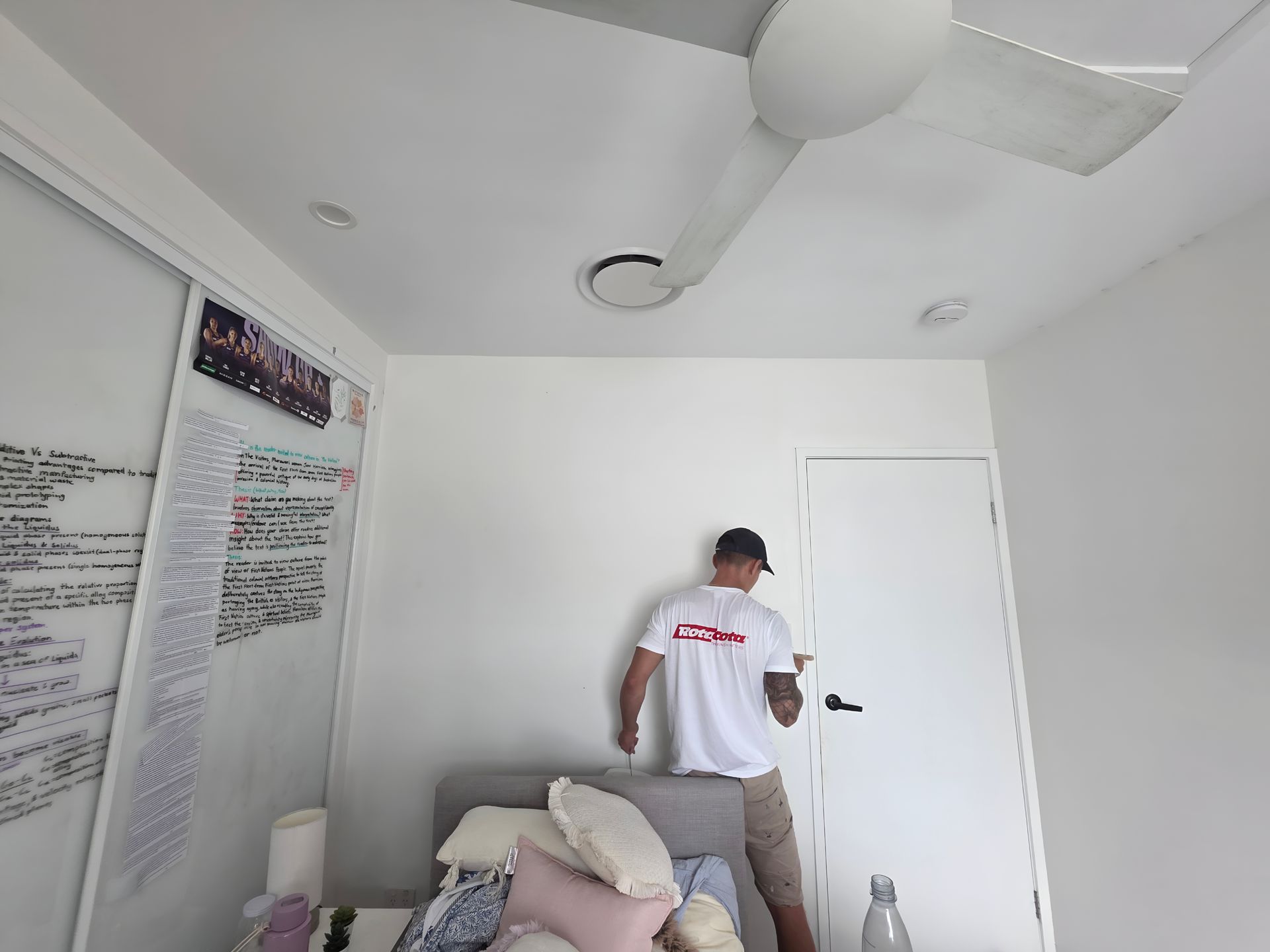 A person wearing a white t-shirt and shorts near a white door, indoors.