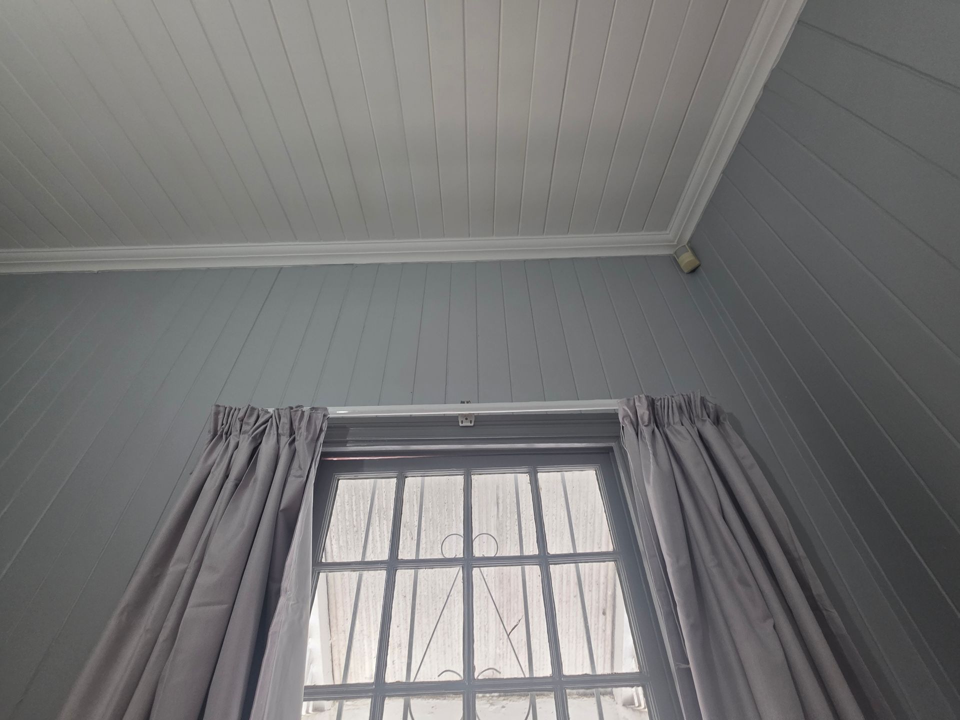 Interior view of a window with curtains, surrounded by grey paneled walls and a white ceiling.