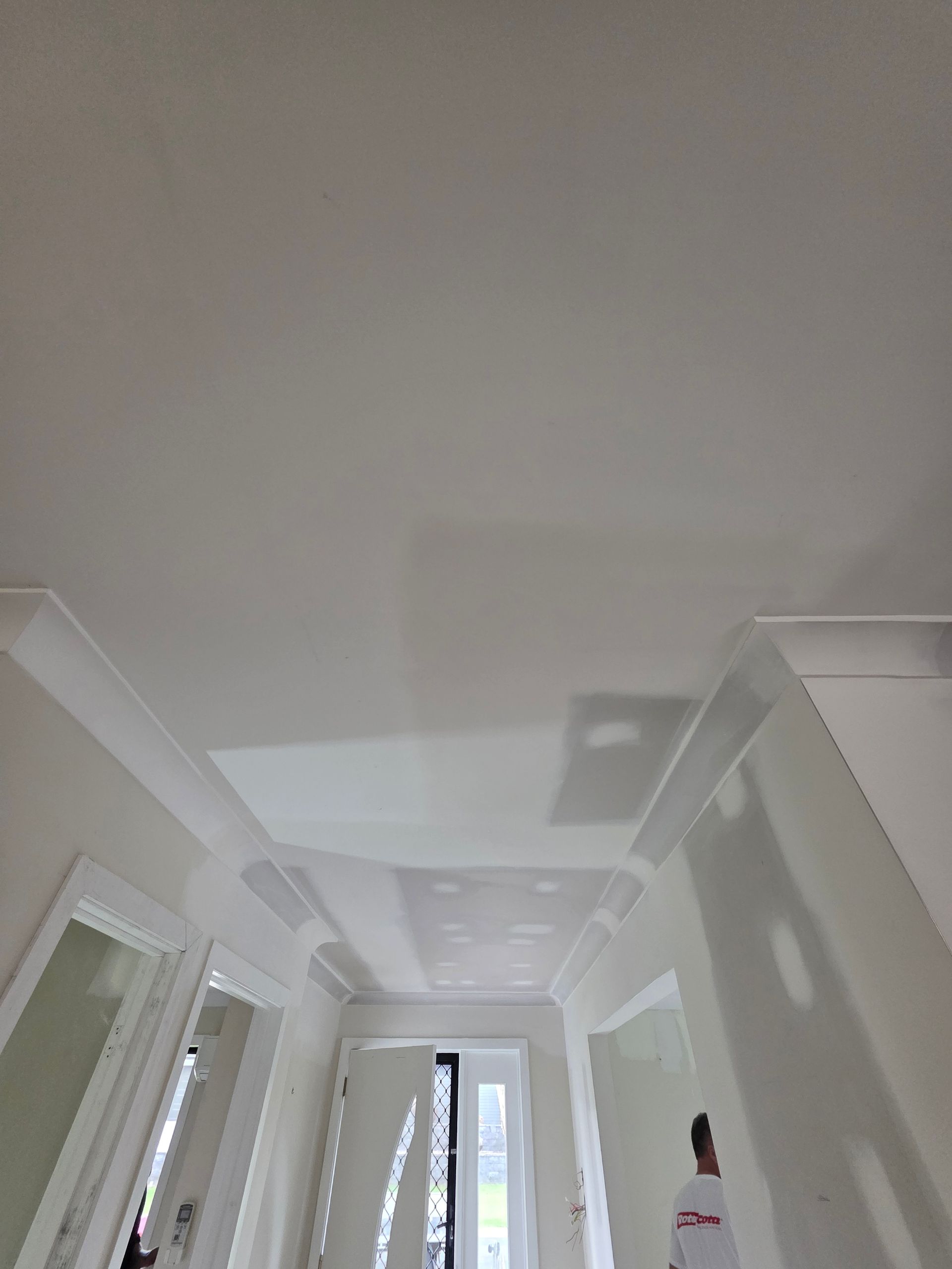 White hallway with crown molding, doors, and a person in the background.