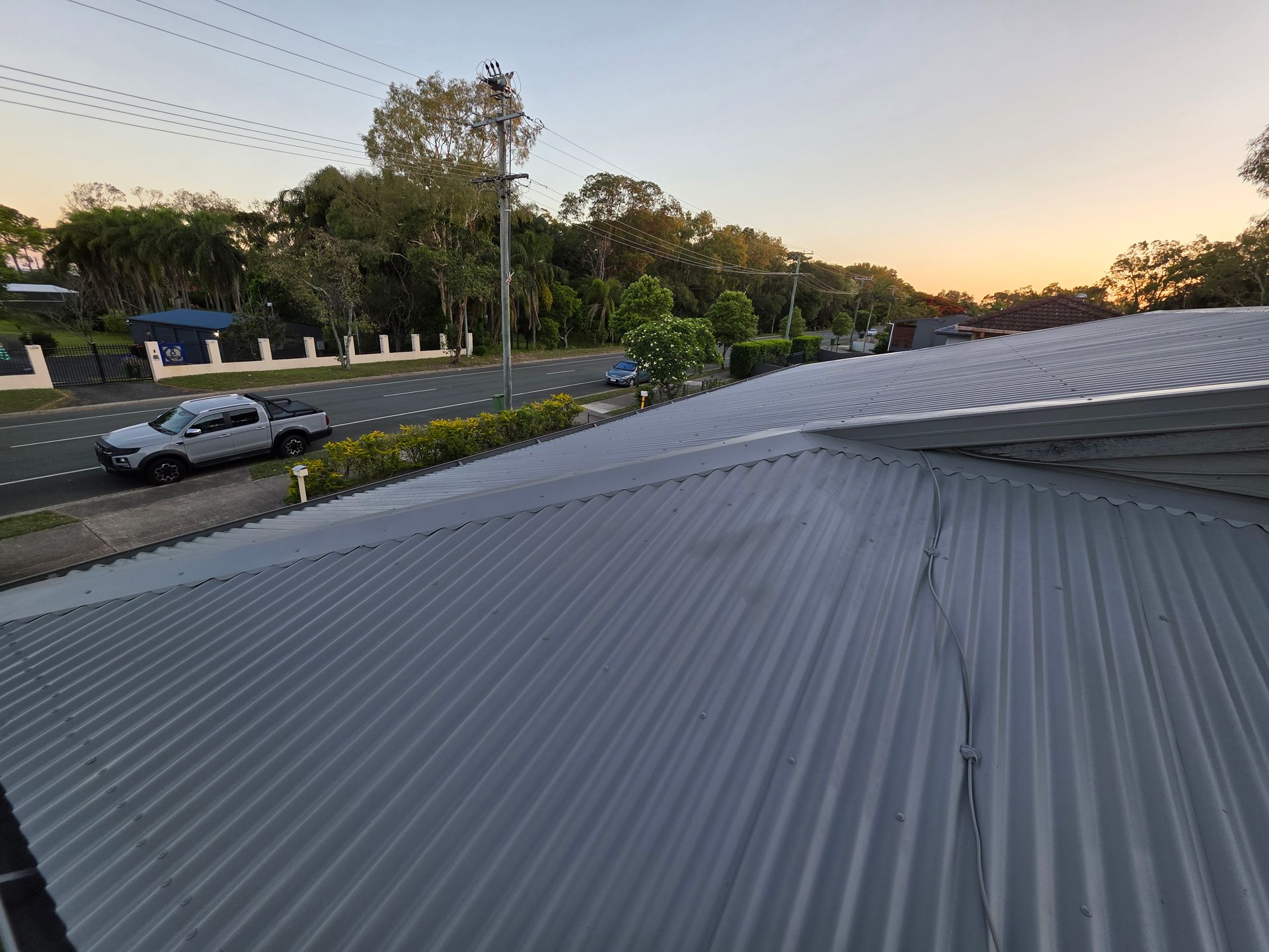 Gray corrugated metal roof with a road and parked cars in the background at sunset.