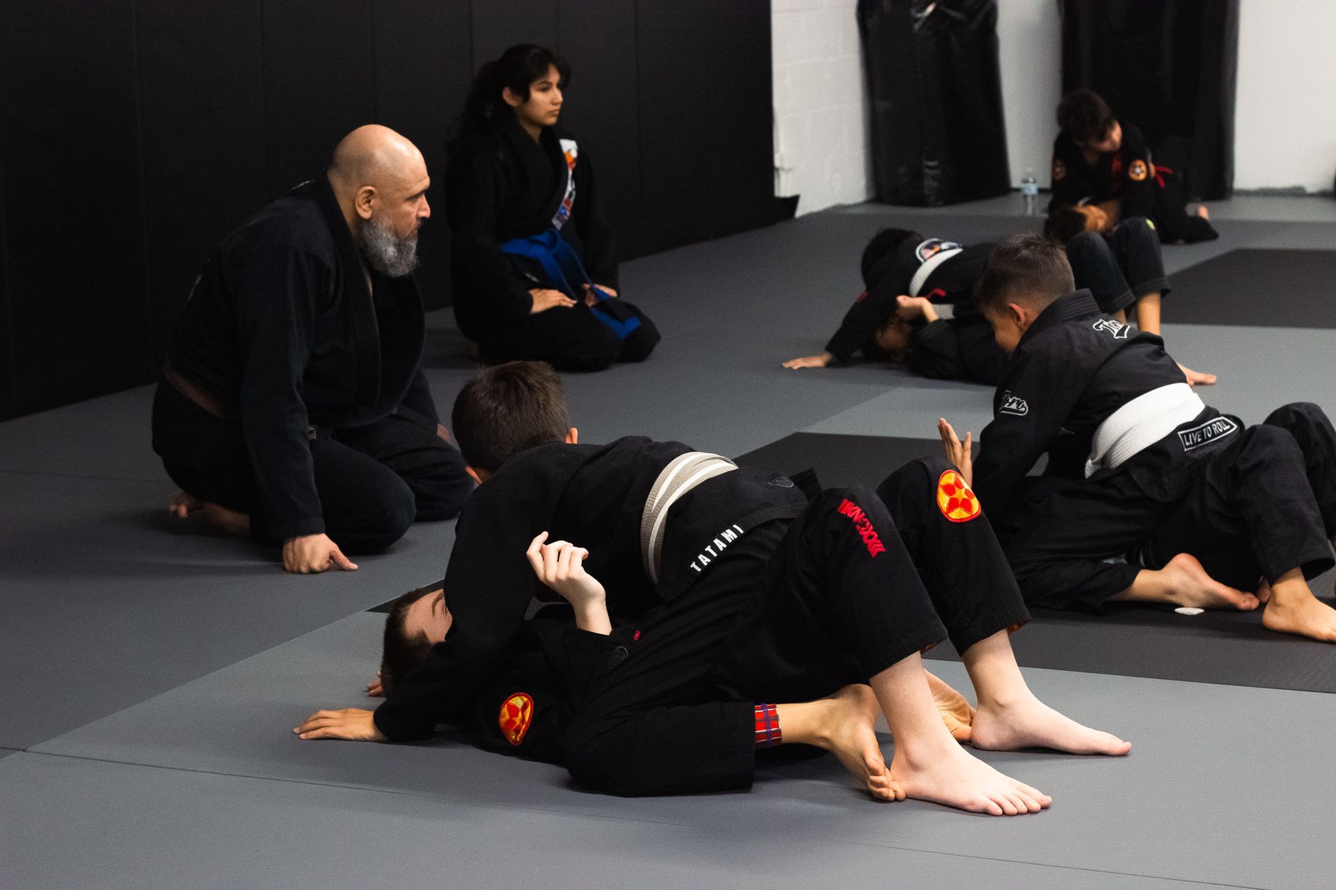 Two people in martial arts uniforms practice a hold in a dojo.