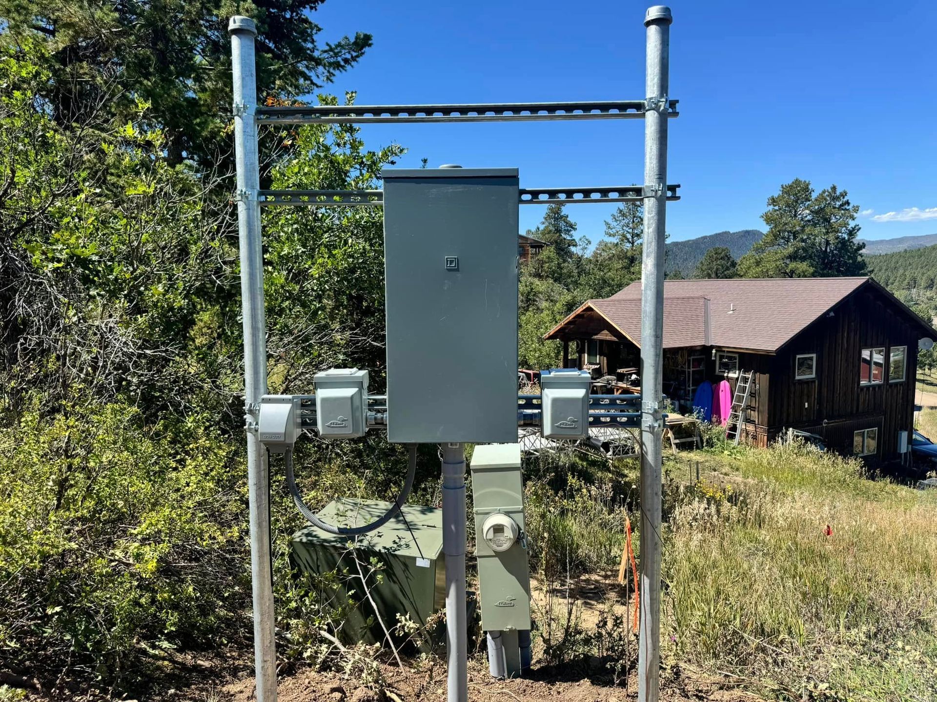 A power box is sitting in the middle of a field in front of a house.