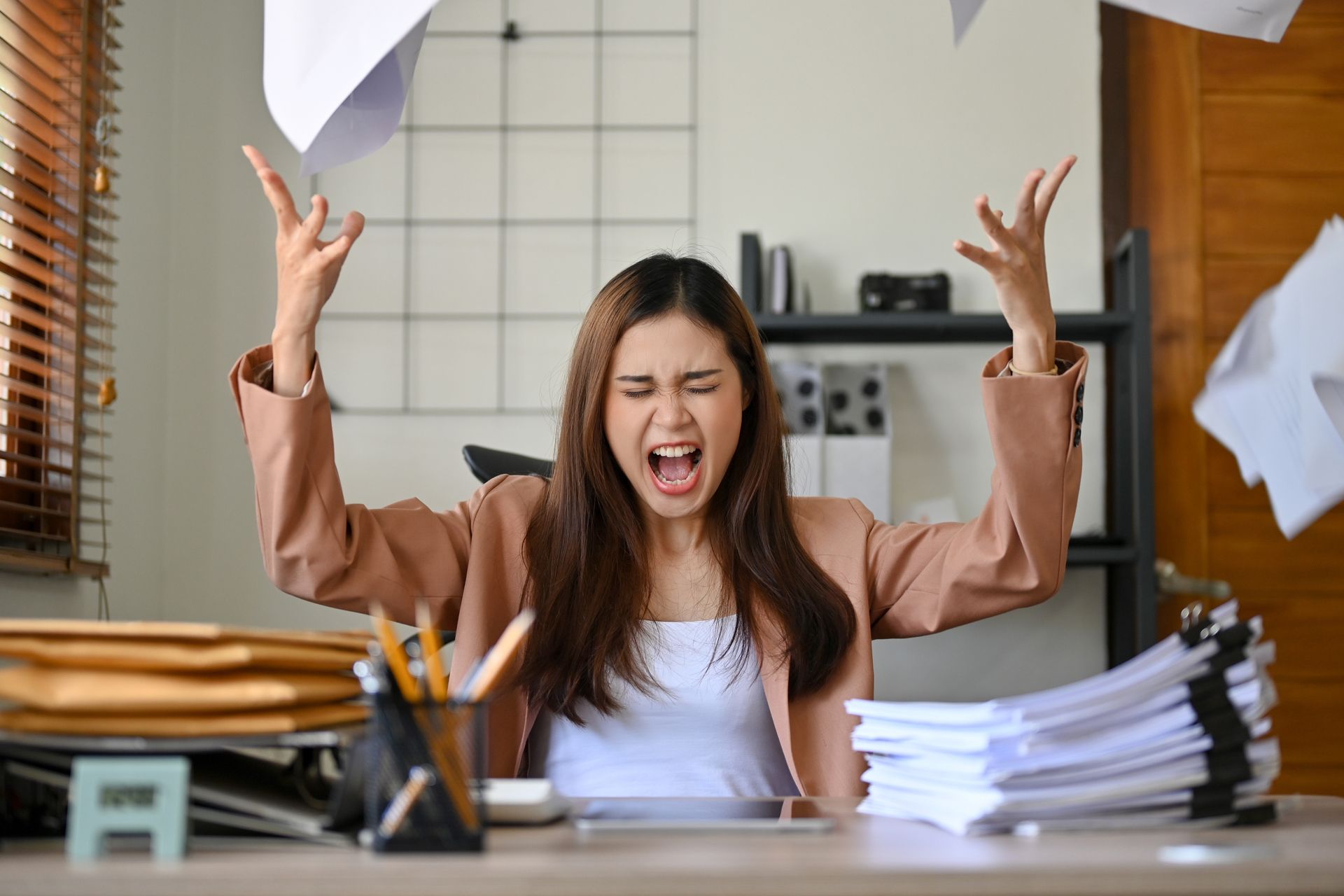 Woman at desk, frustrated, throwing papers in the air.