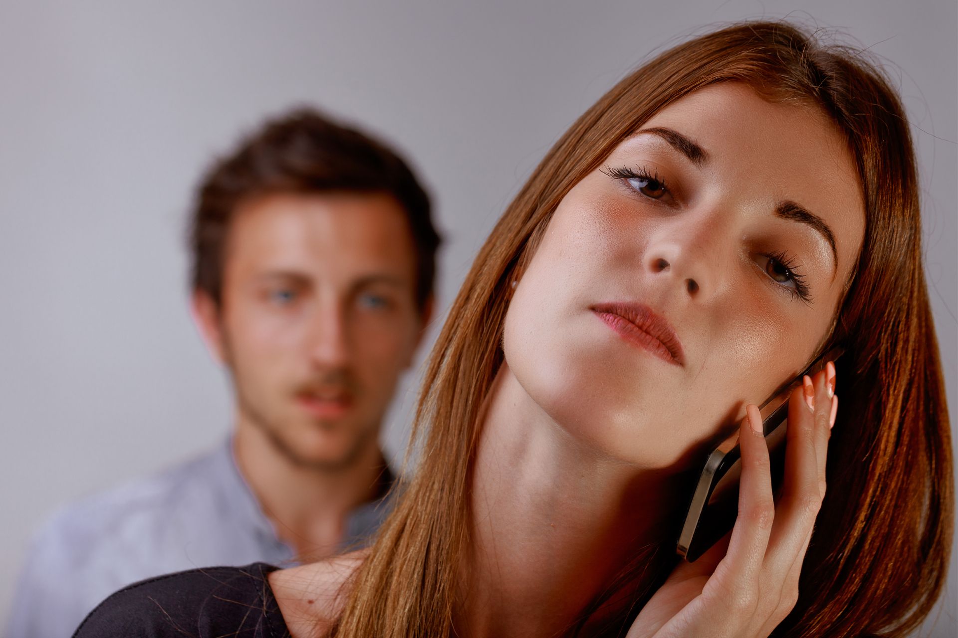Woman on phone, man behind looking concerned.