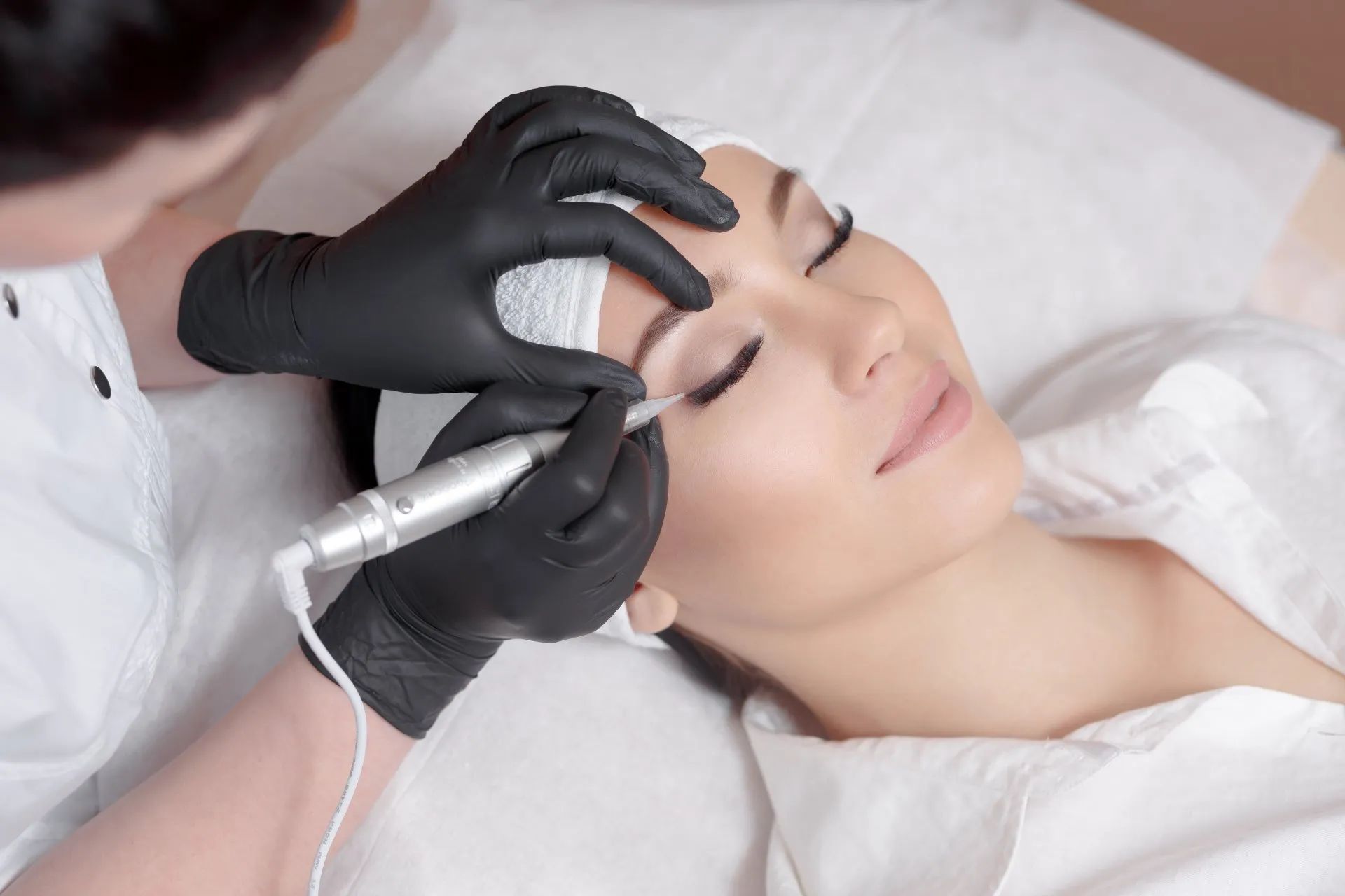 a woman is getting her eyebrows done by a woman wearing black gloves