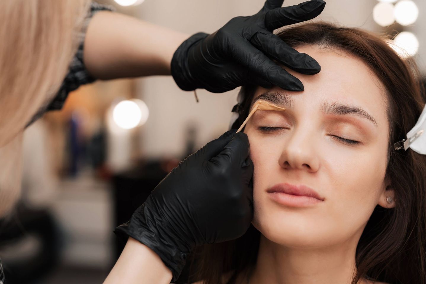 a woman is getting her eyebrows waxed by a woman wearing black gloves