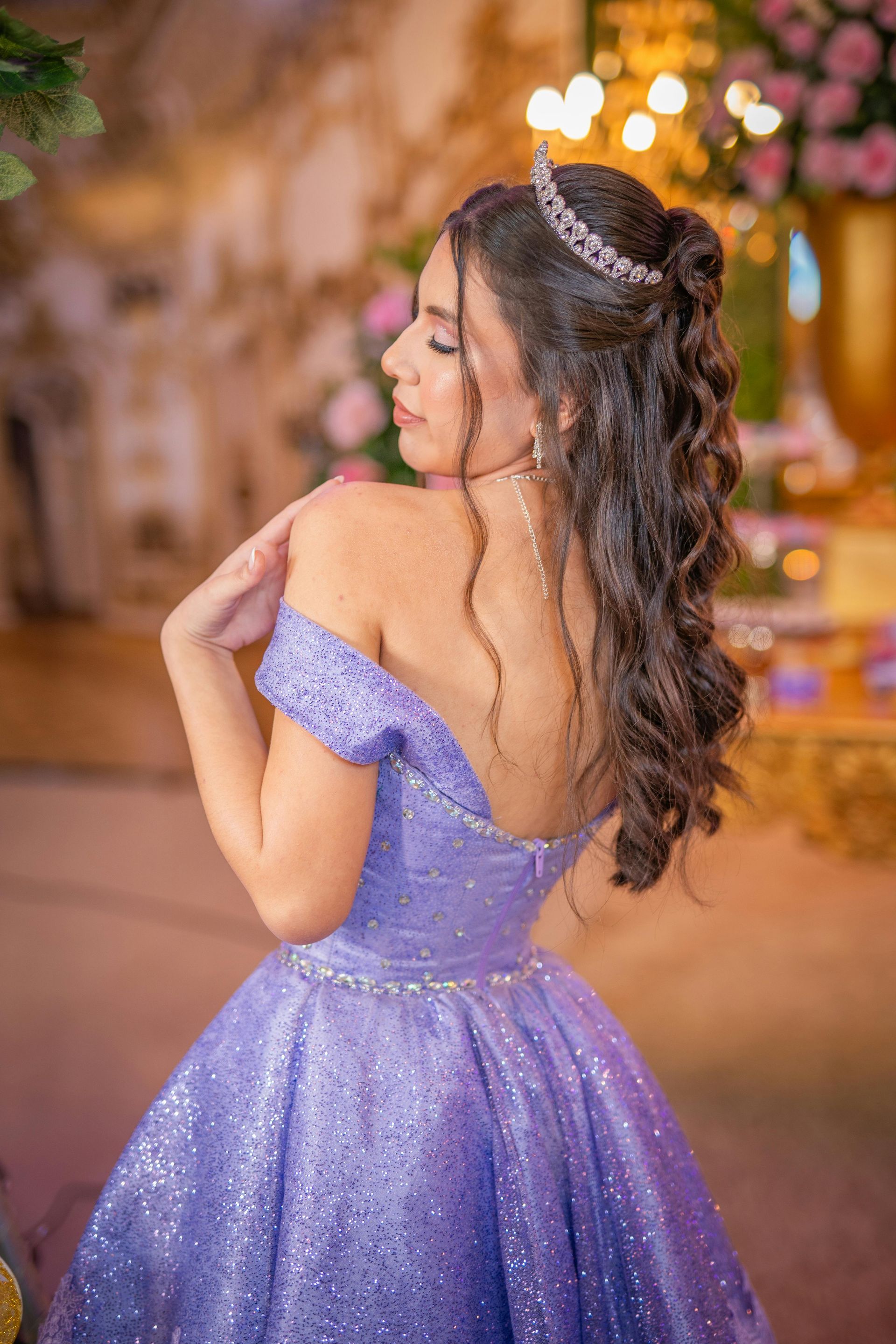 Young woman in a lavender glitter gown and tiara, smiling slightly, at a party.