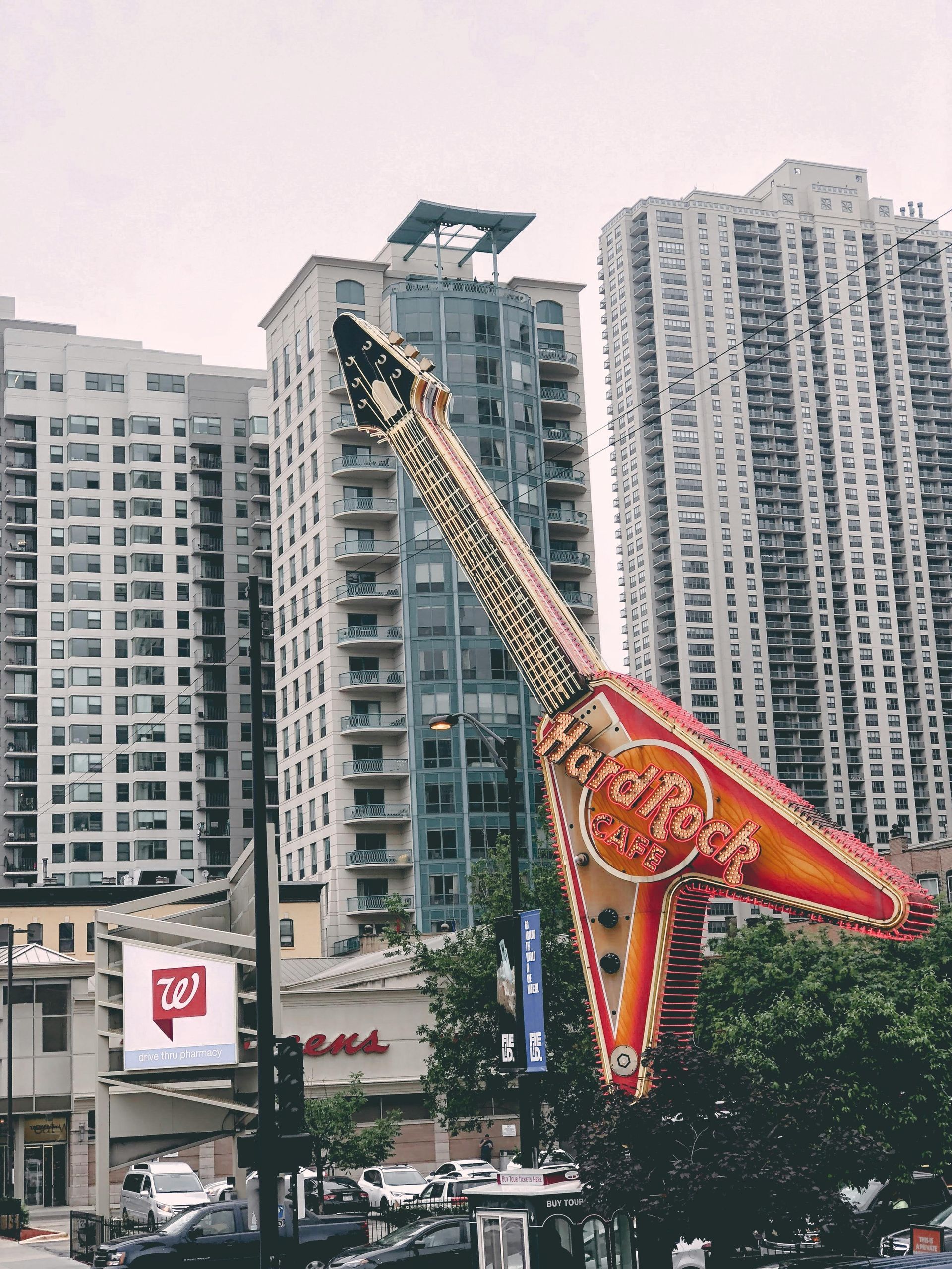 Giant Hard Rock Cafe guitar sign in front of buildings and a cloudy sky.