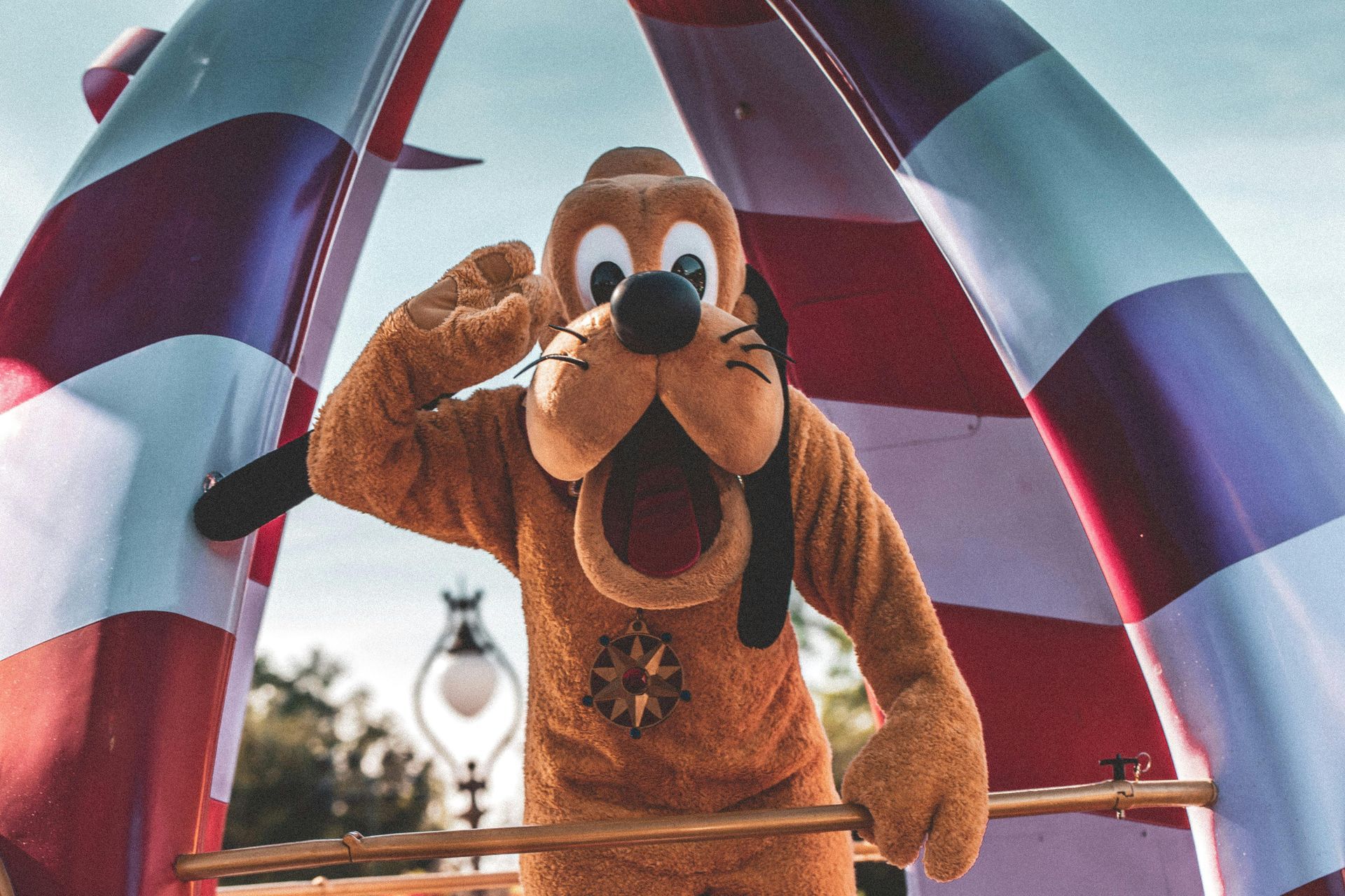 Pluto salutes, standing in a red and white striped structure at Disneyland.