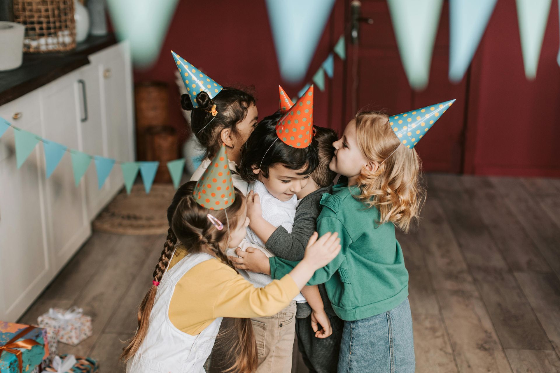 Children in party hats hug, celebrating at a party.