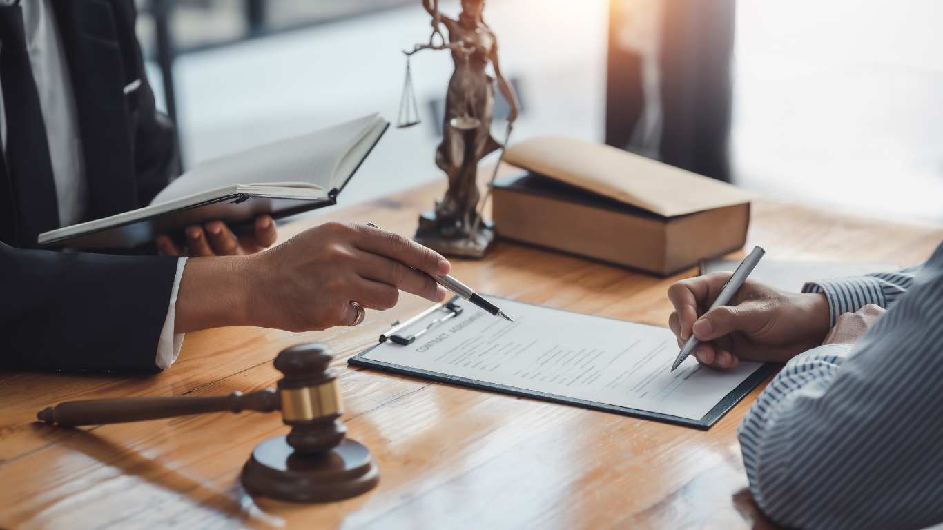 a lawyer is sitting at a table with a client signing a document .