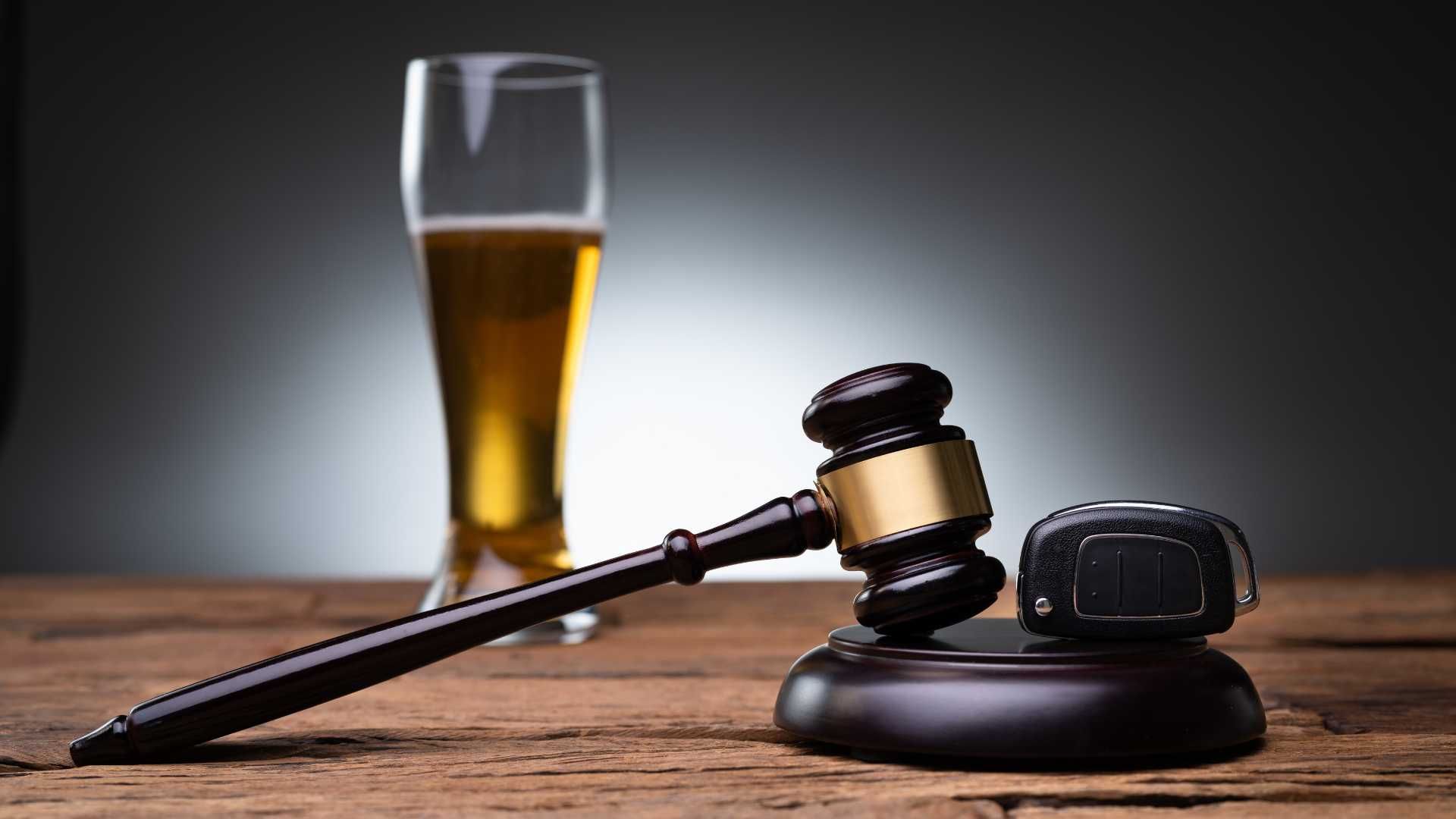 a glass of beer , a judge 's gavel and a car key on a wooden table .