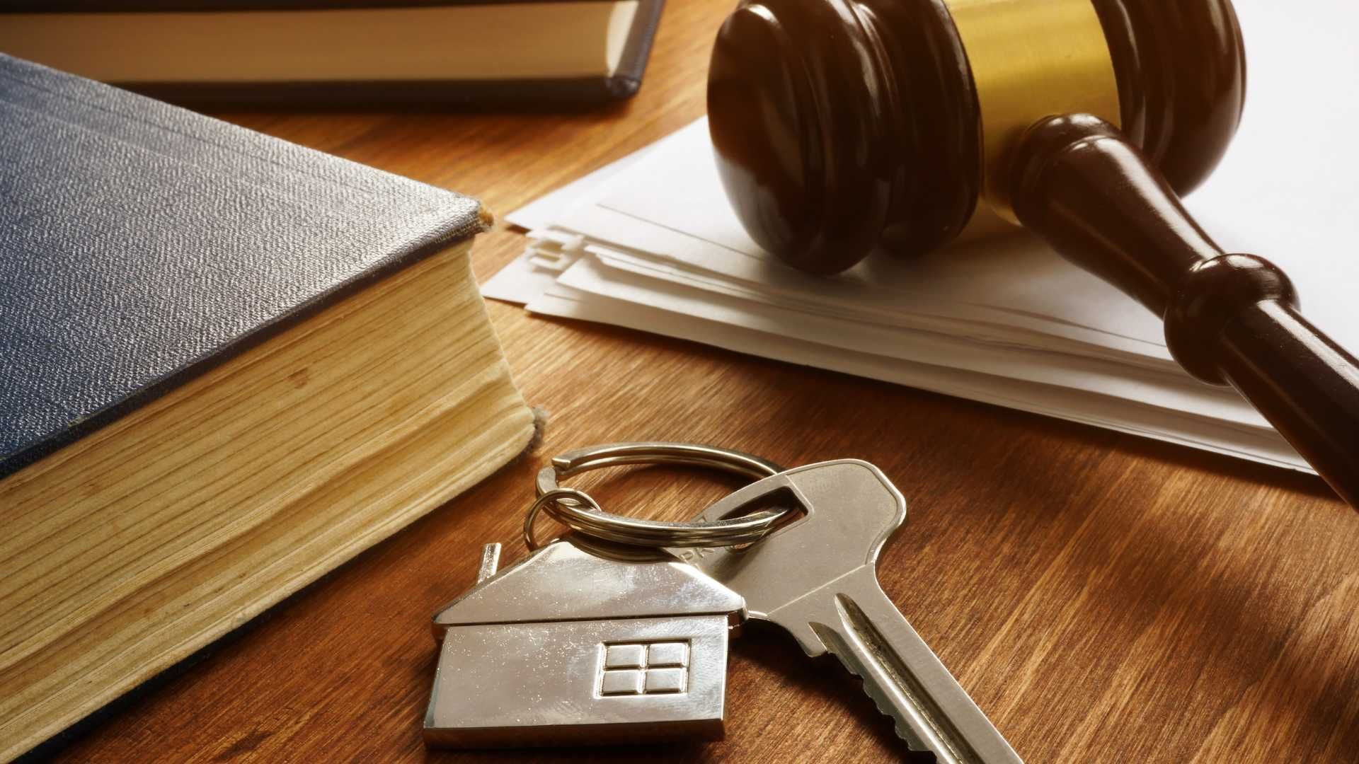 a pair of keys sitting on top of a wooden table next to a book and a judge 's gavel .