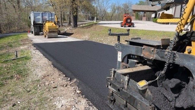 A machine is laying asphalt on a road next to a house