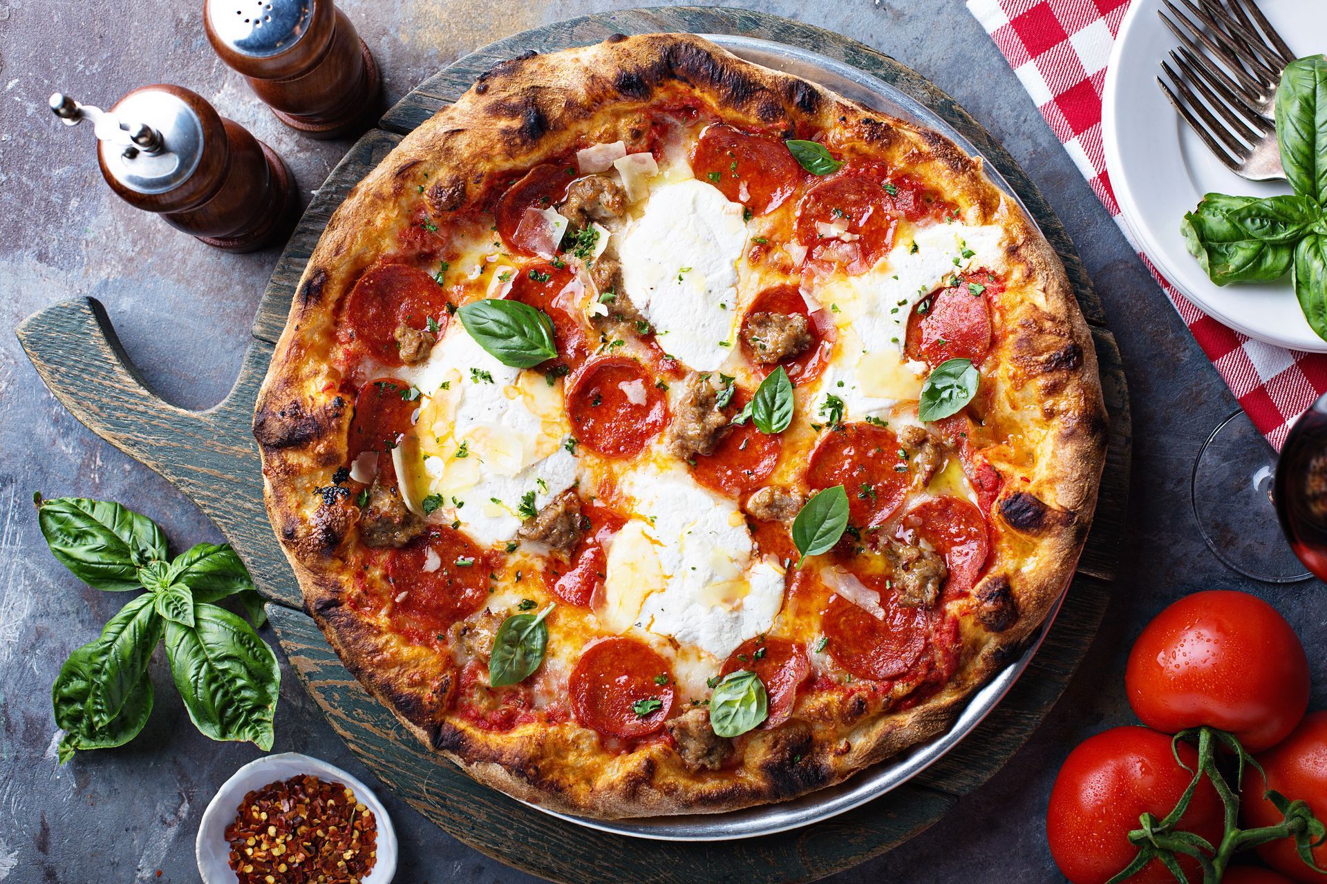 Cheese pizza with basil and tomatoes on a rustic table, with fresh ingredients around it