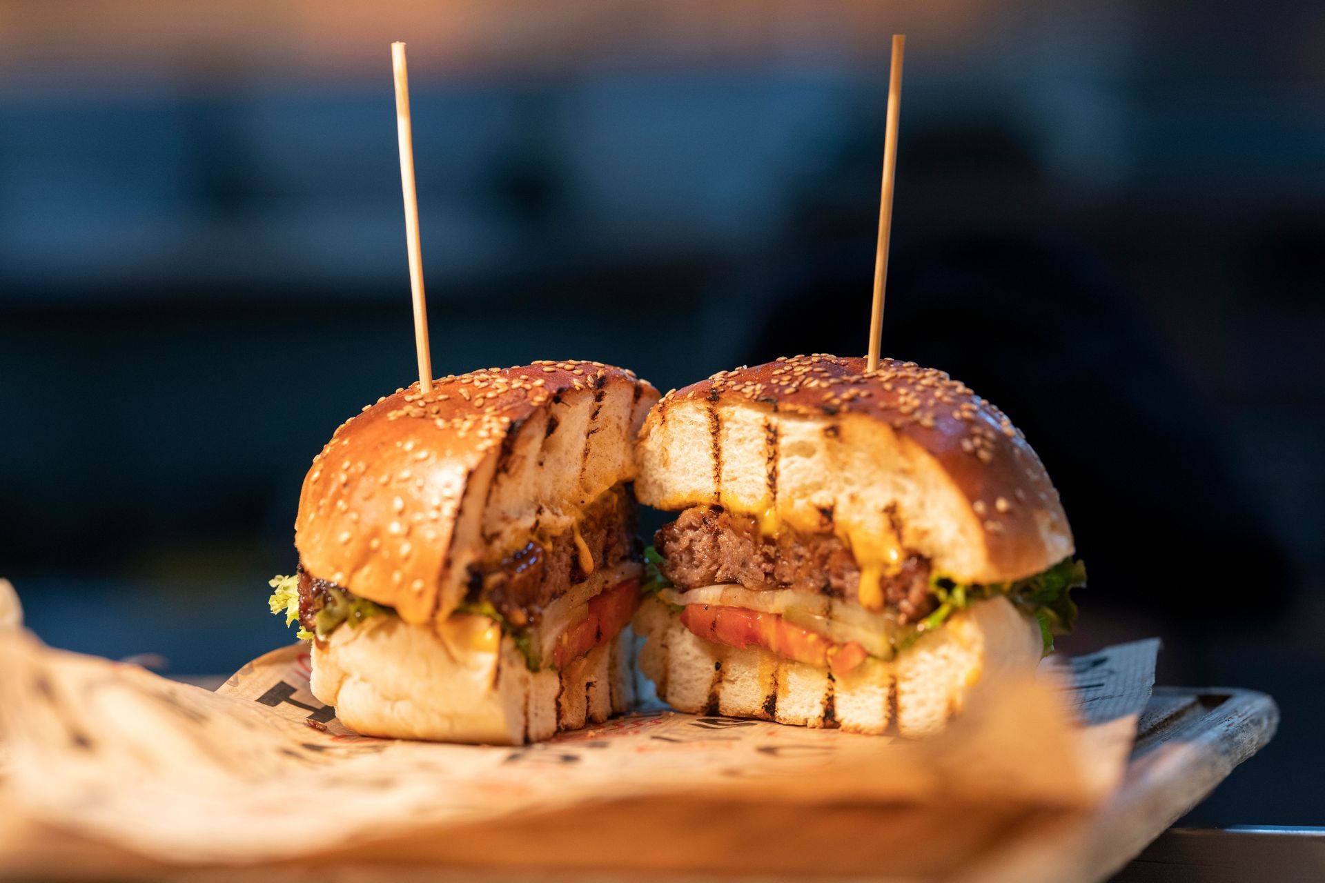 Close-up of a sliced burger sandwich with toothpicks on a wooden board, blurred background