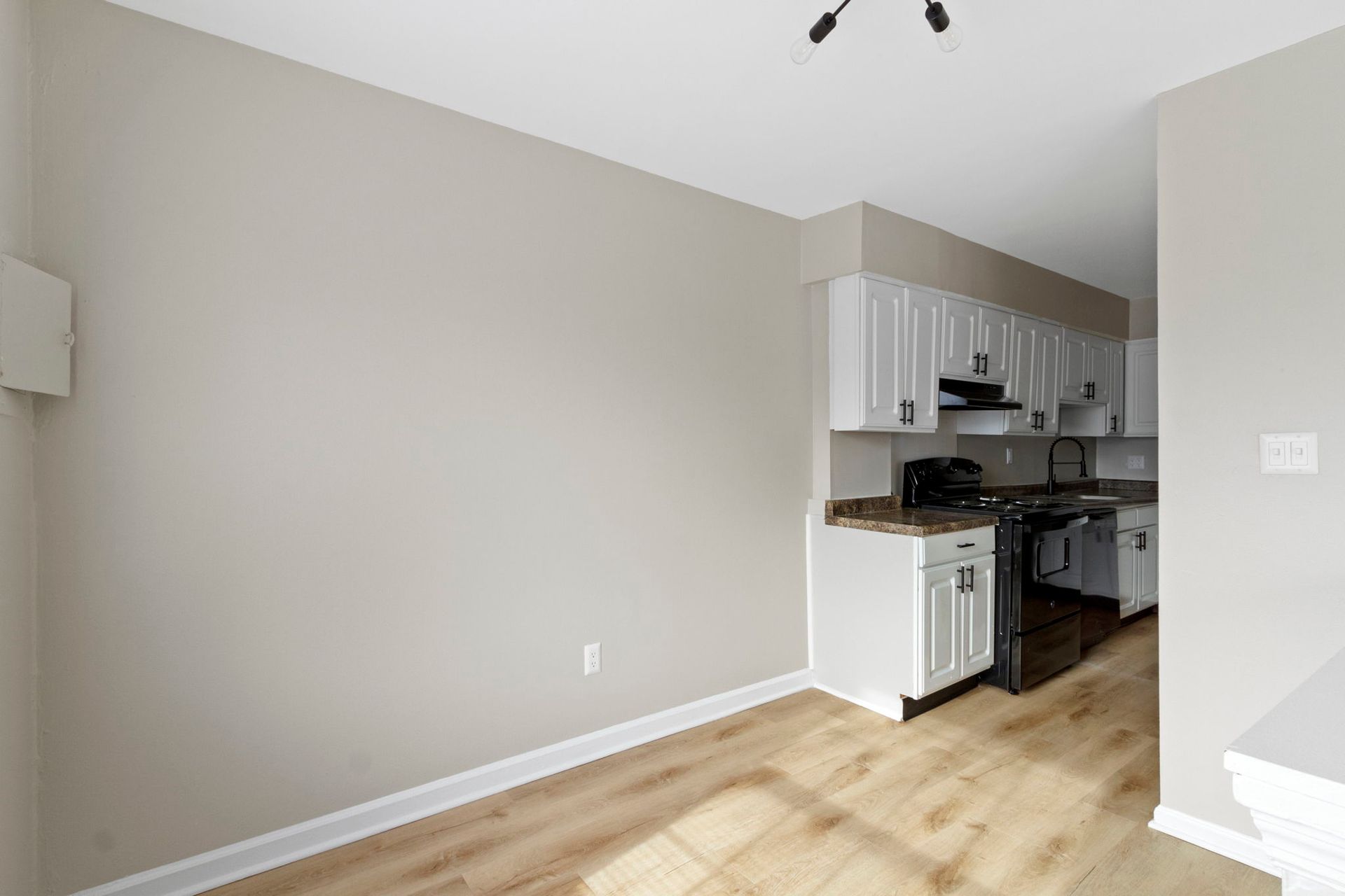 Empty beige dining room with a view into a white kitchen and black appliances.