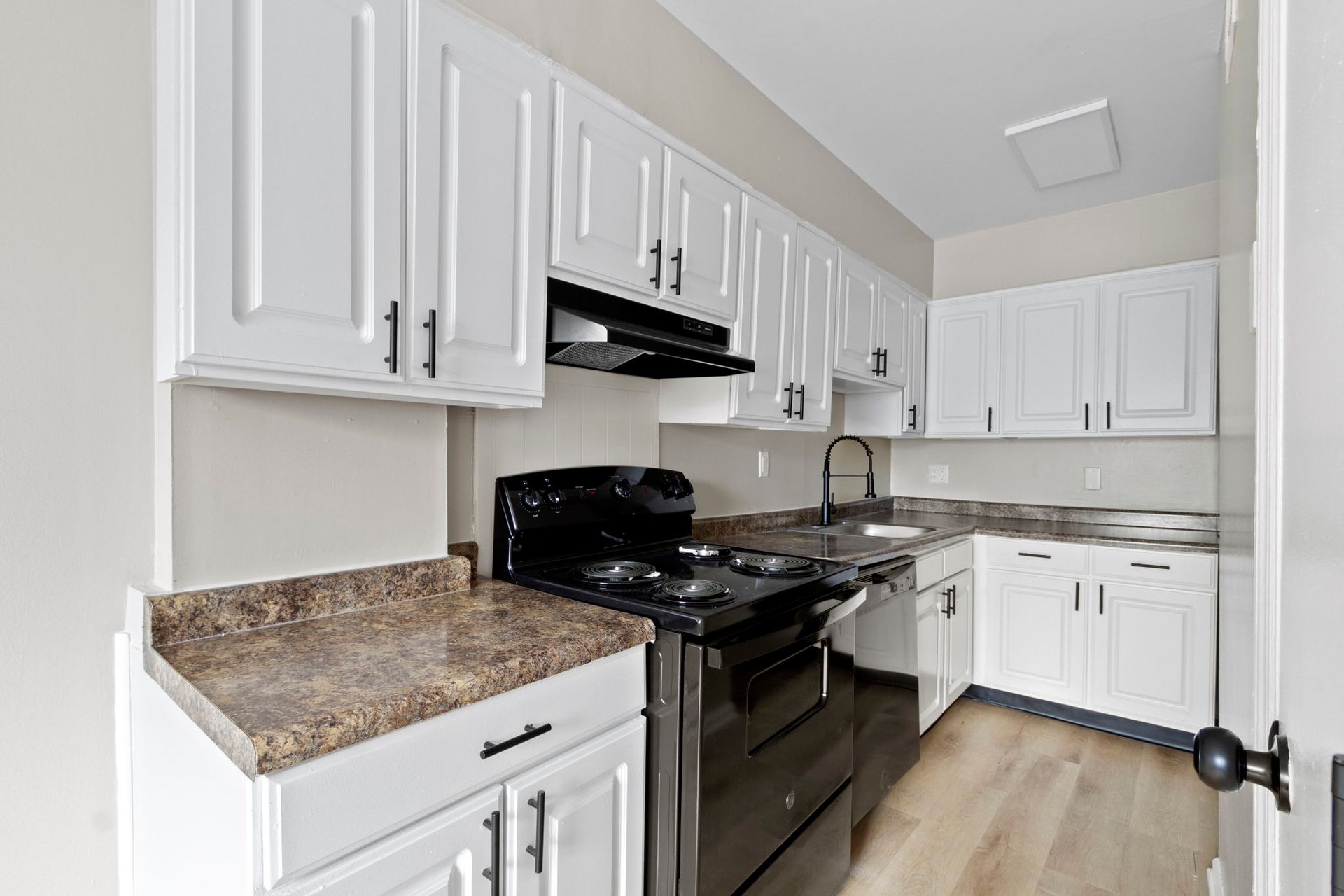 White kitchen cabinets with black appliances and countertops.