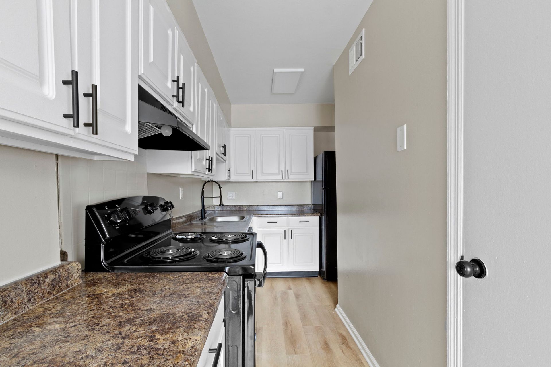 White kitchen with black appliances and hardware; view down the narrow space.
