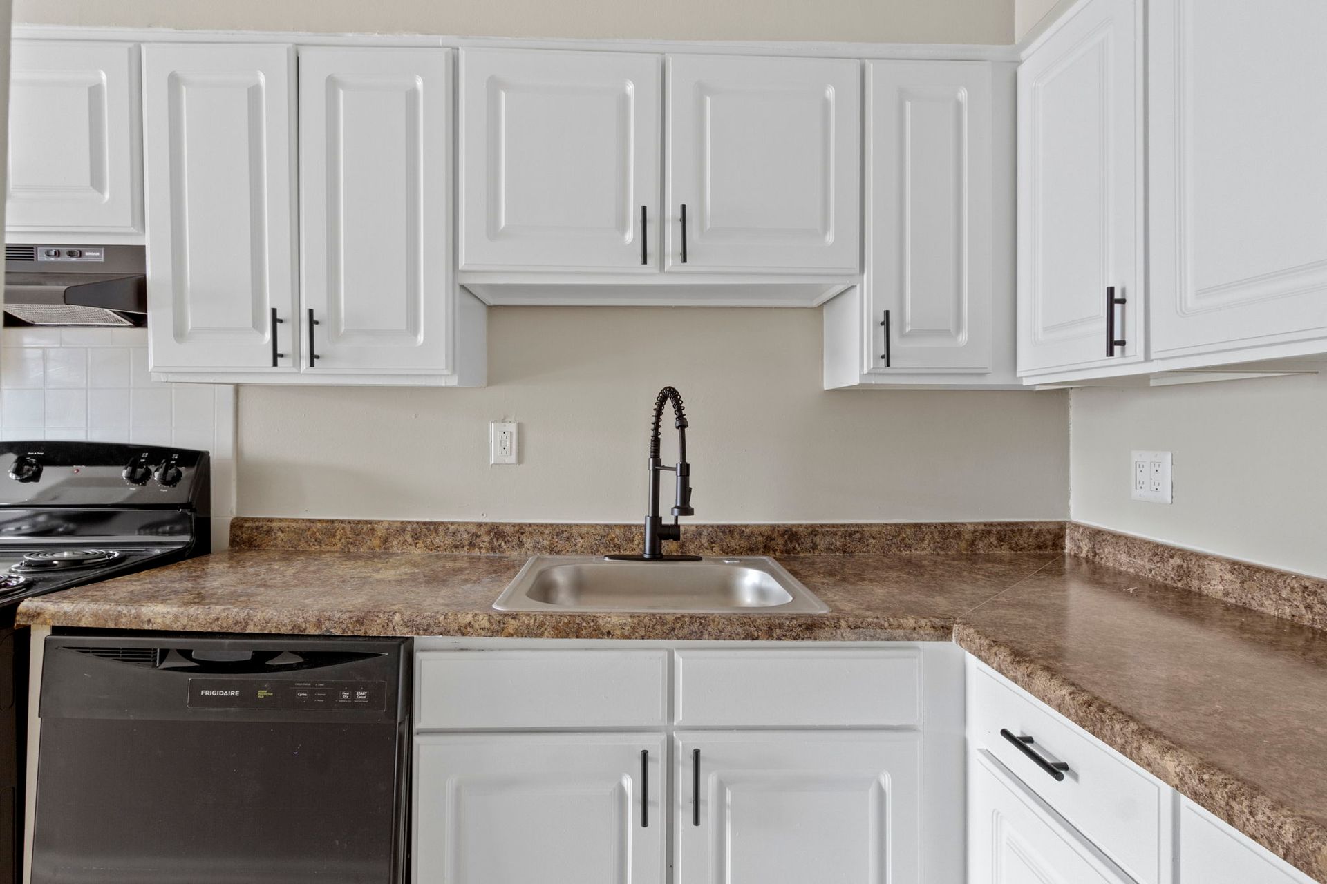 White kitchen cabinets with black hardware, brown countertops, and a black faucet.