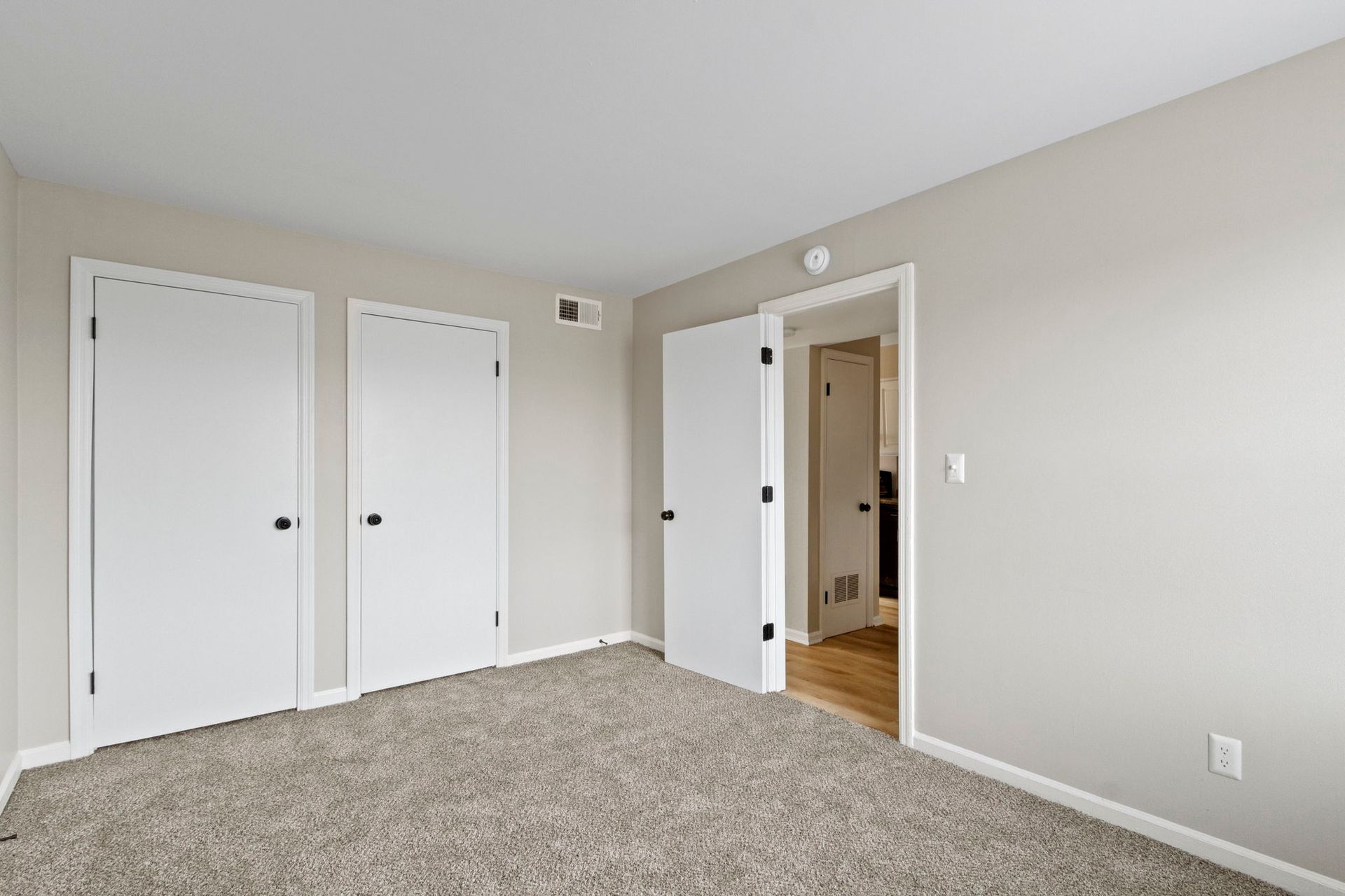 Empty bedroom with three white doors, gray carpet, and light gray walls.