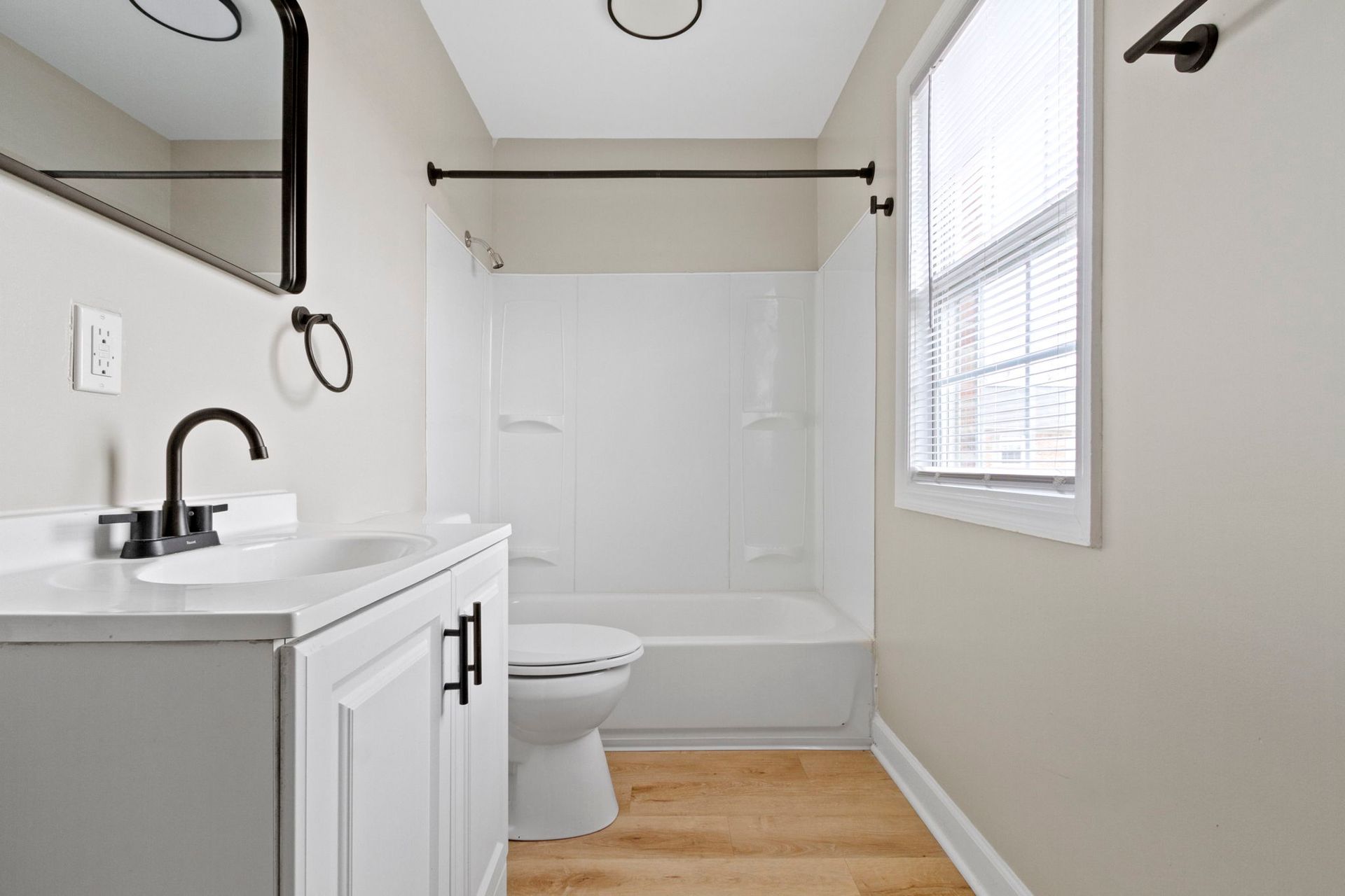 Bathroom with white vanity, toilet, shower, and window. Black fixtures and neutral walls.