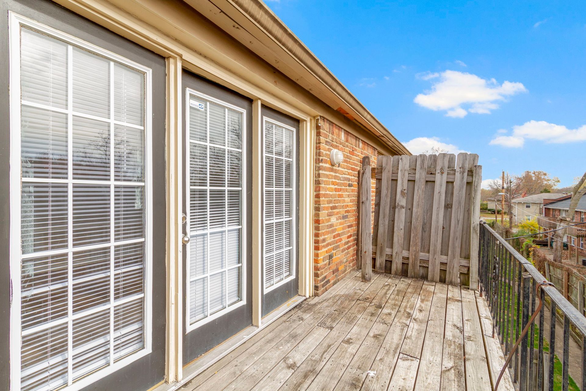 Balcony with French doors and wooden fencing; brick wall and blue sky.