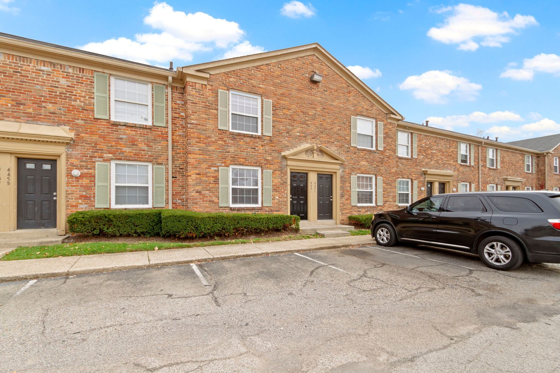 Red brick townhomes with green shutters and a black SUV parked out front.