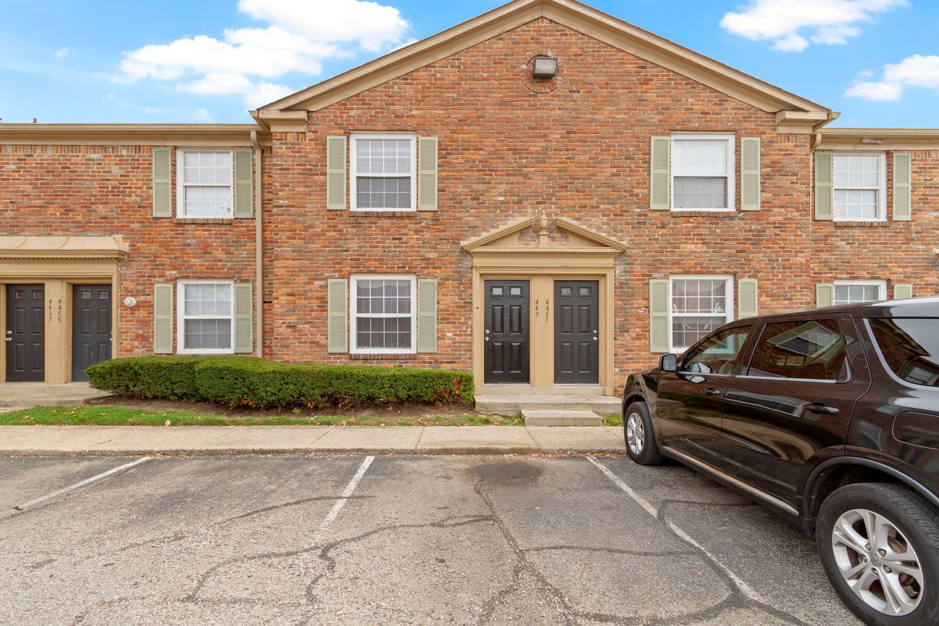 Brick apartment building with black doors and a parked SUV.
