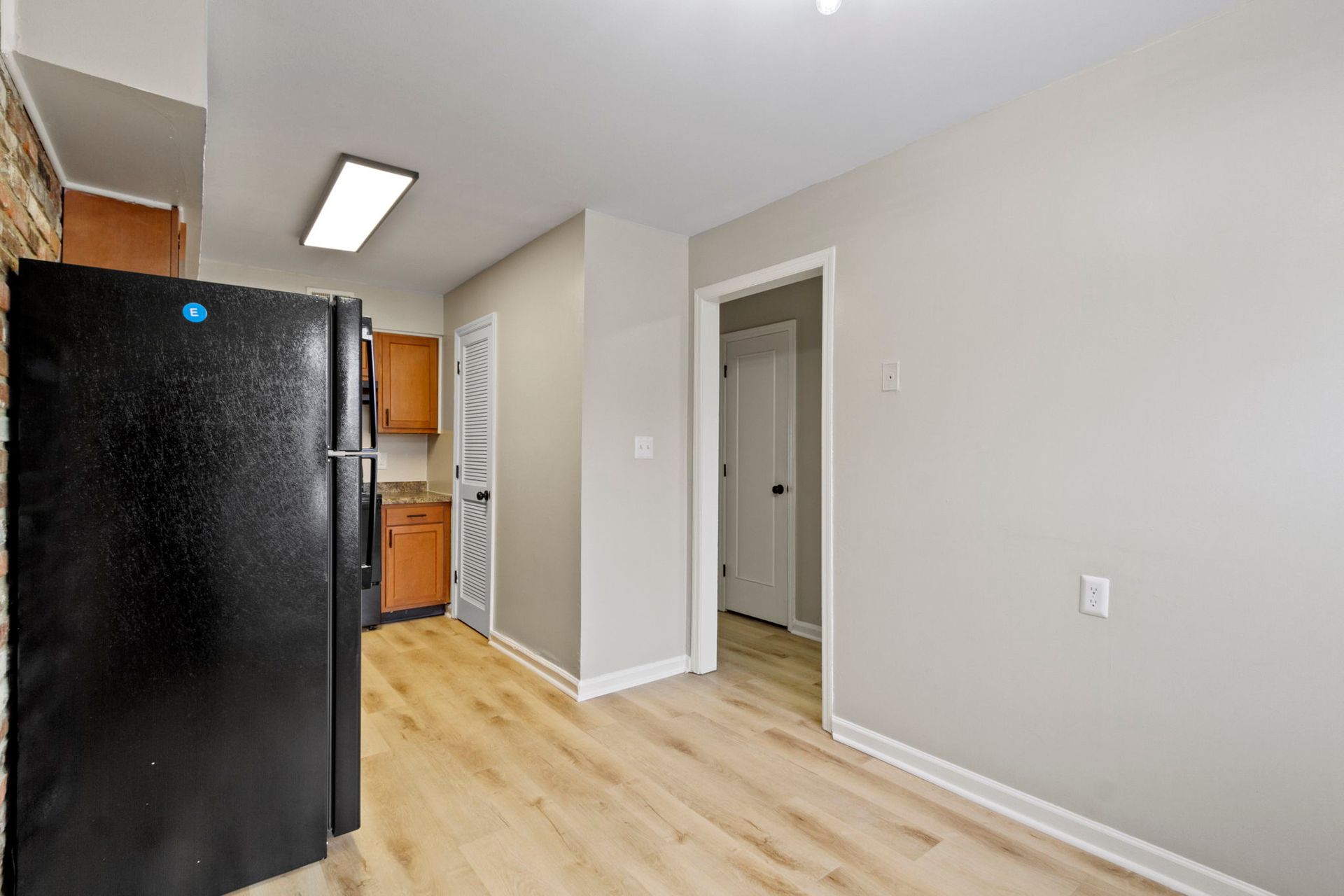 Kitchen with black fridge, wooden cabinets, and light wood flooring.  A doorway and laundry-style door.