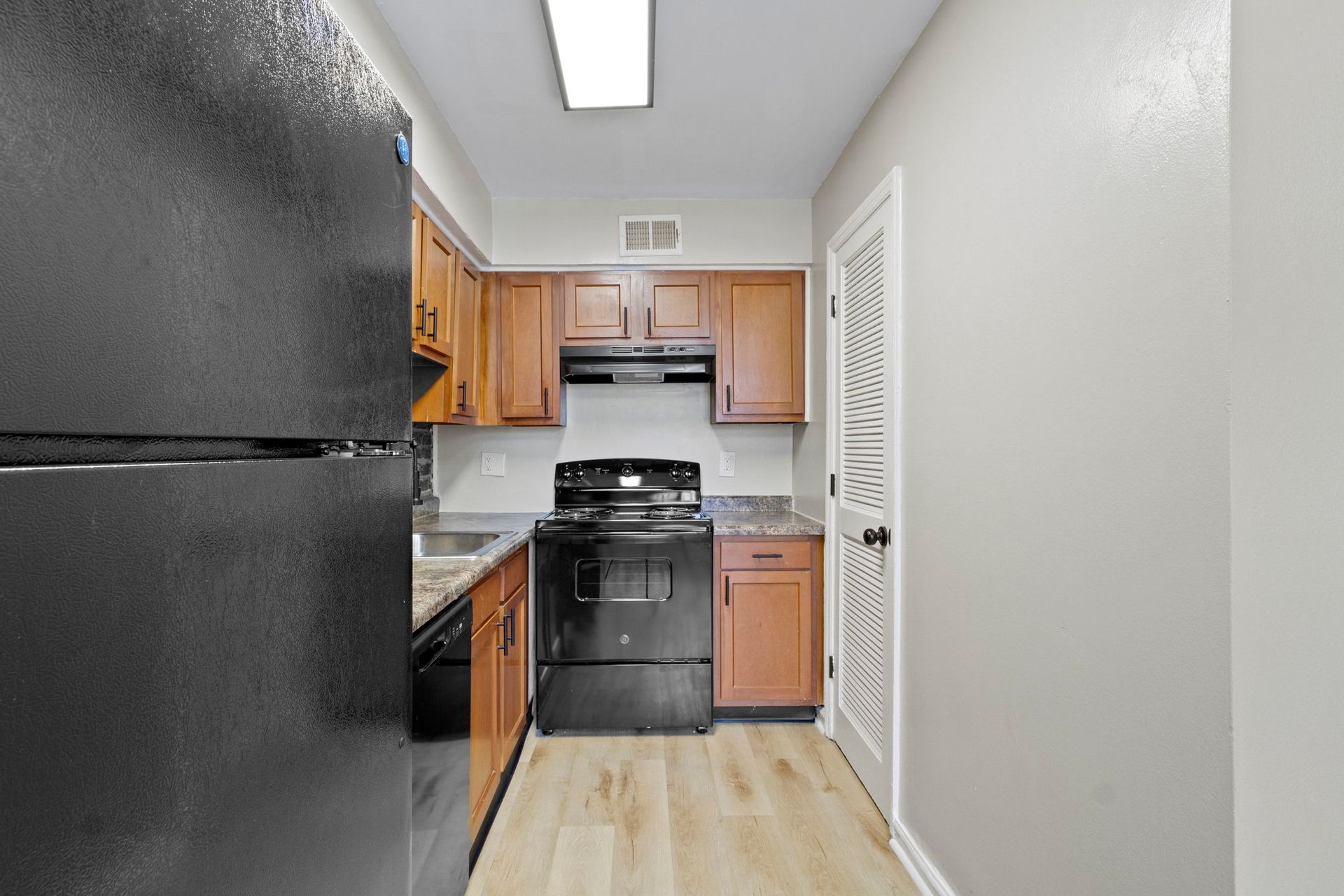 Kitchen with black appliances, brown cabinets, beige walls, and light wood-look flooring.