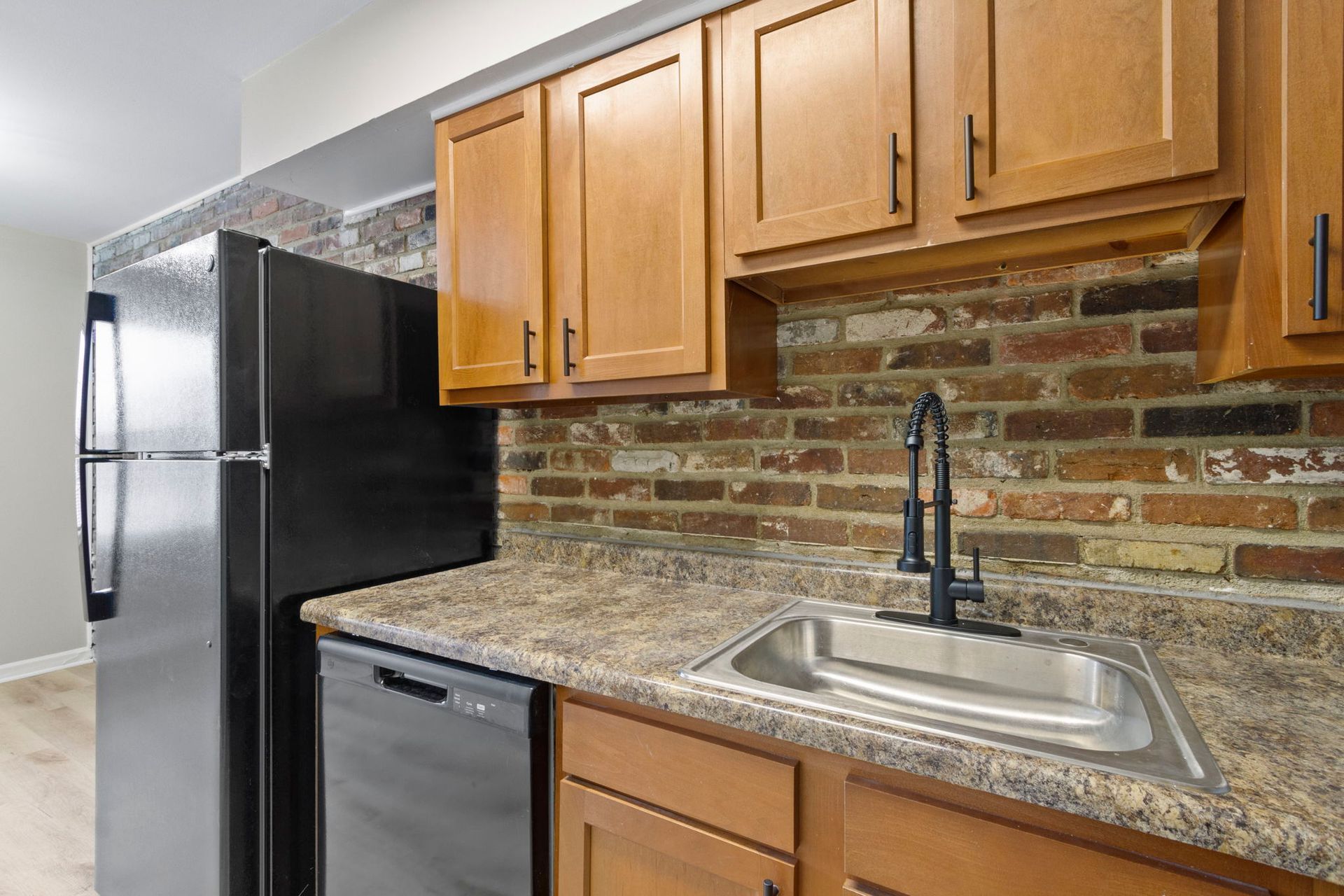 Kitchen with brown cabinets, brick backsplash, stainless steel sink and appliances.