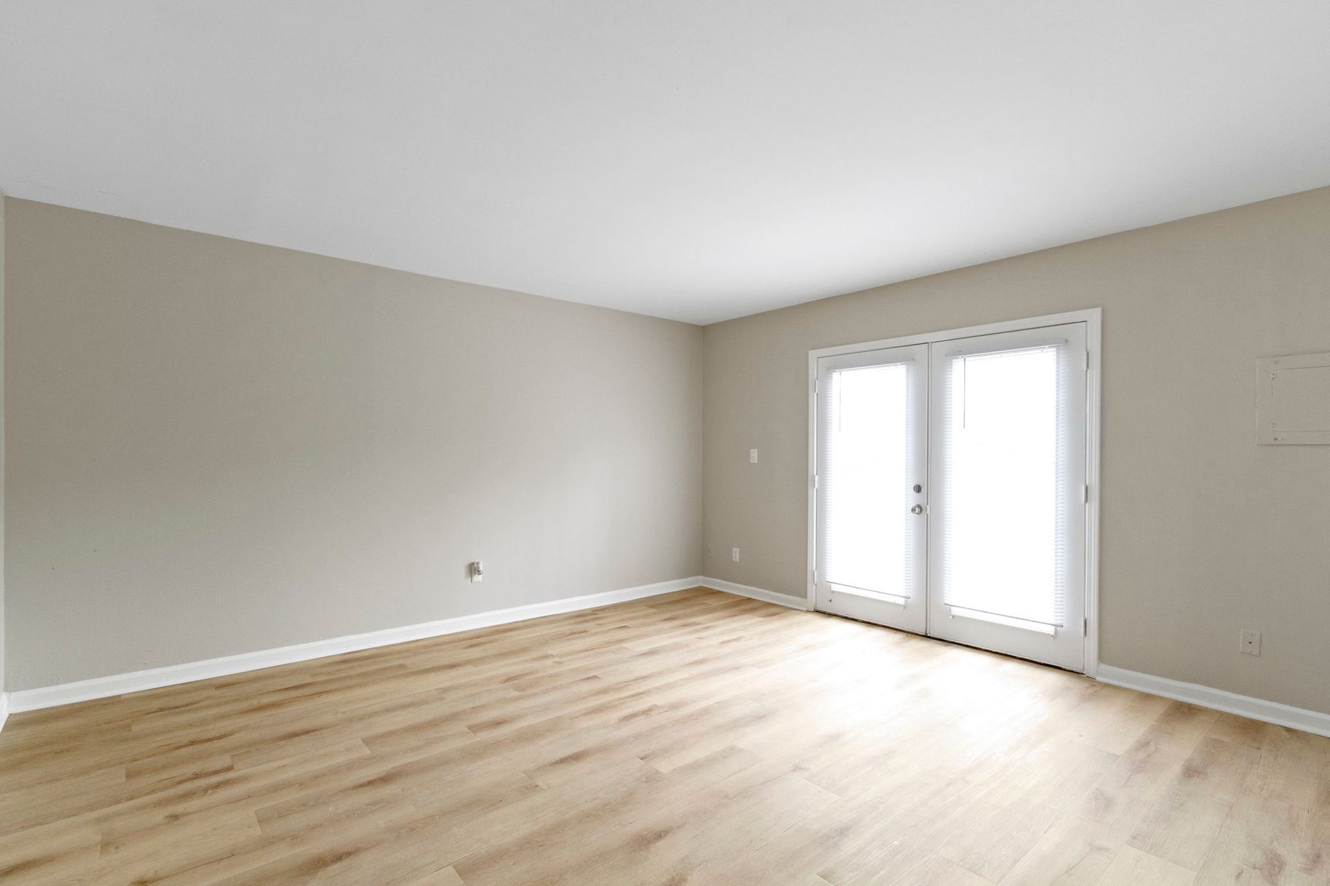 Empty room with wood floors, light beige walls, and French doors leading outside.