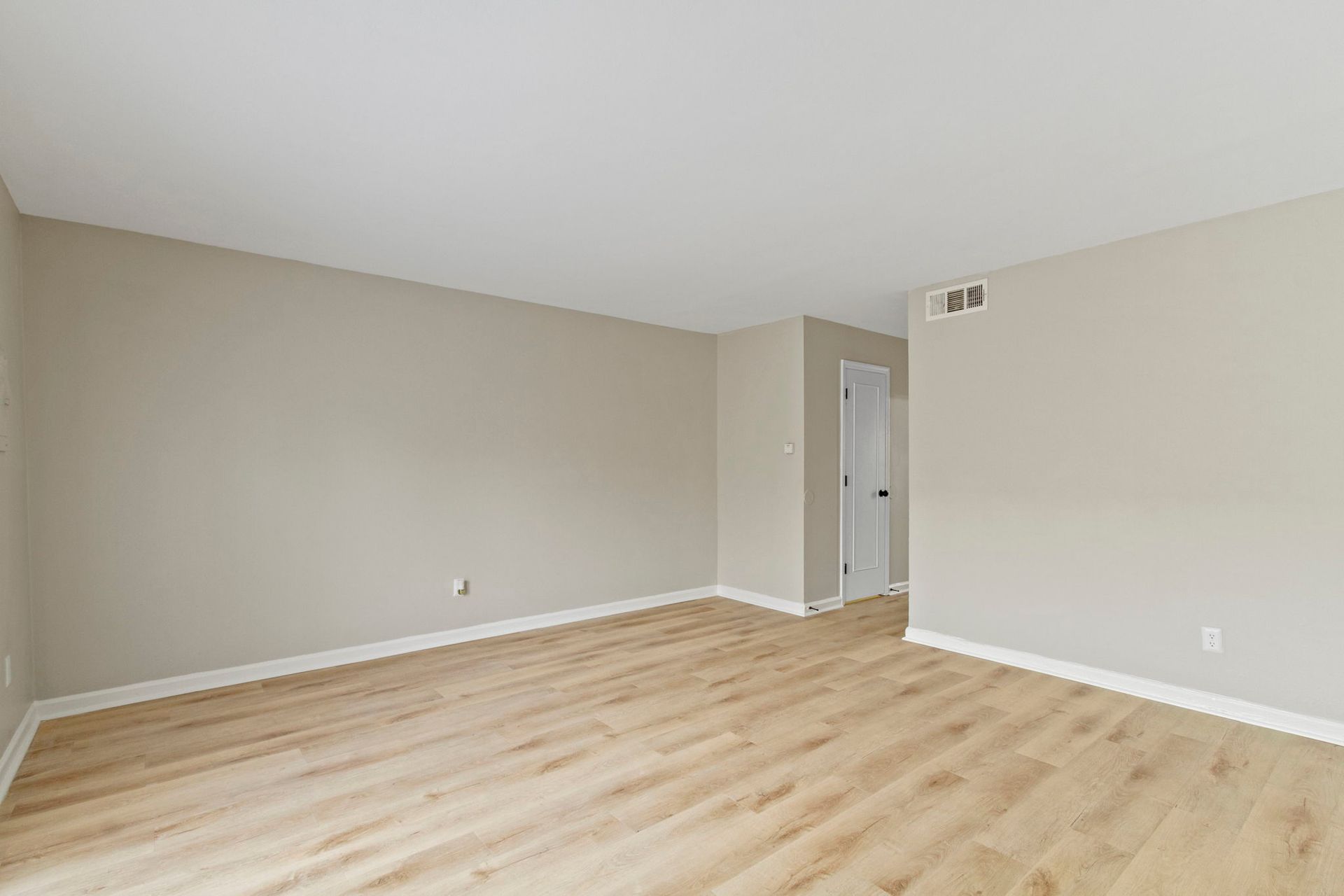 Empty living room with beige walls, light wood floor, and doorway.