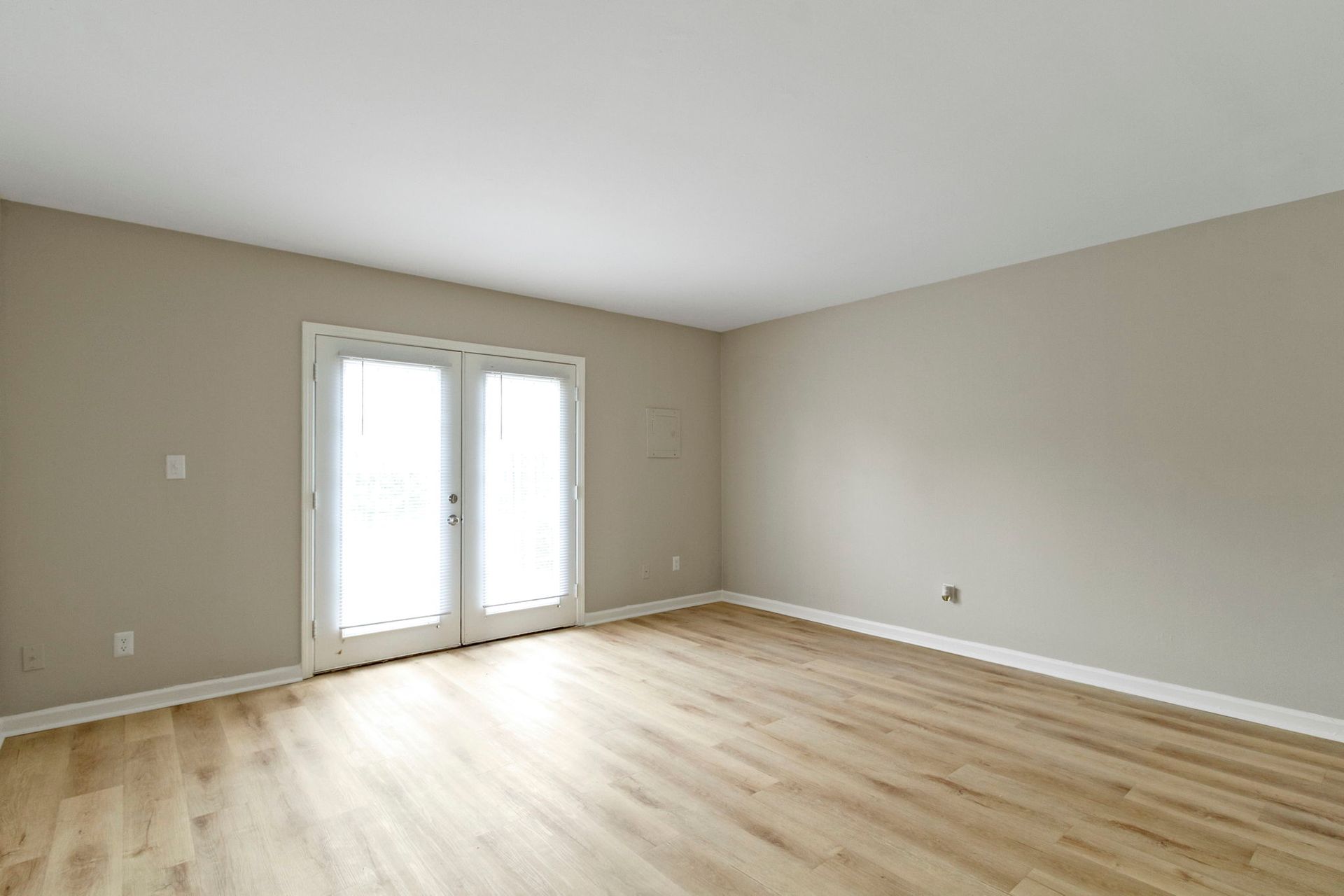 Empty room with French doors, beige walls, wood floors.