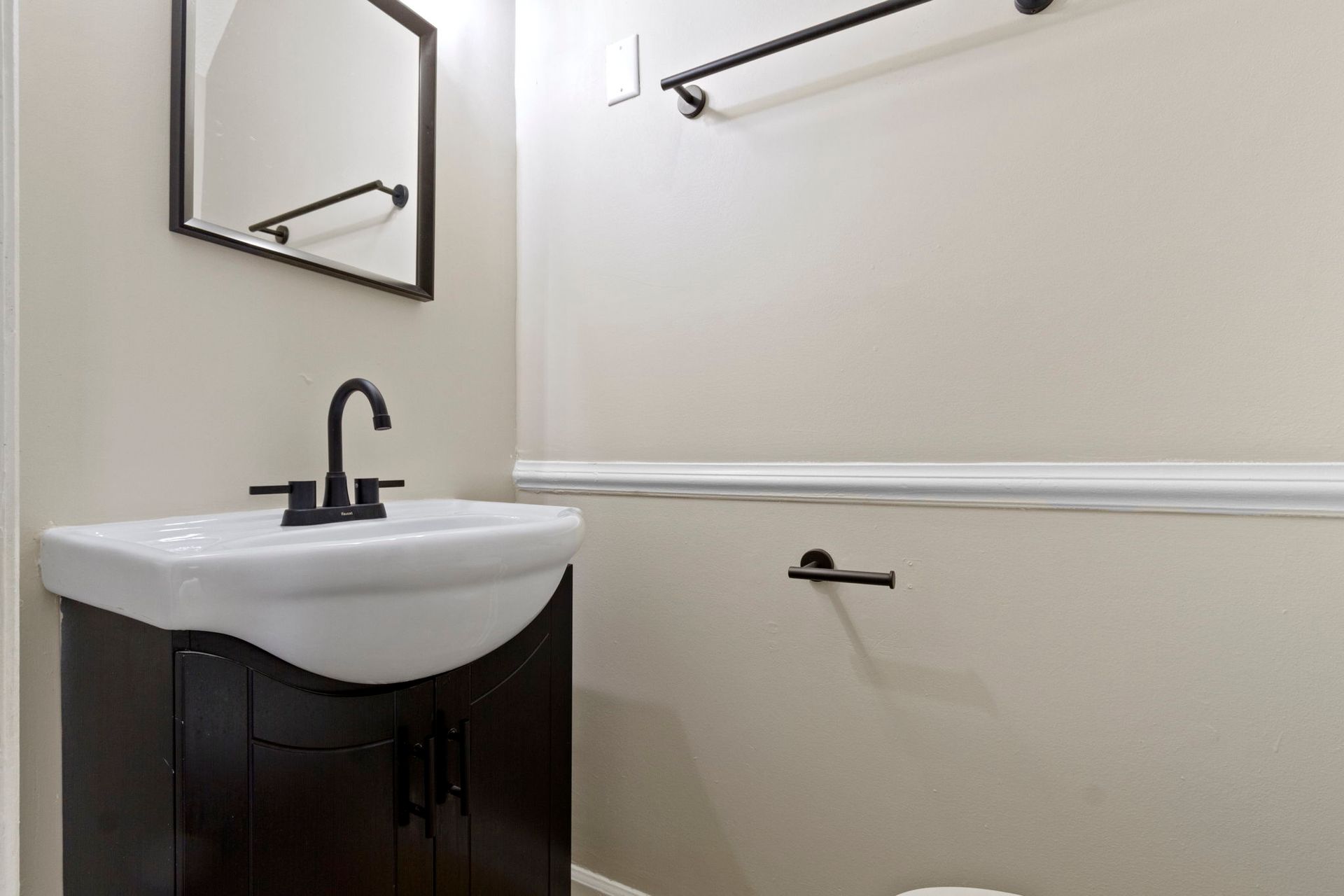 Bathroom with dark wood vanity, black fixtures, and white sink against beige walls.