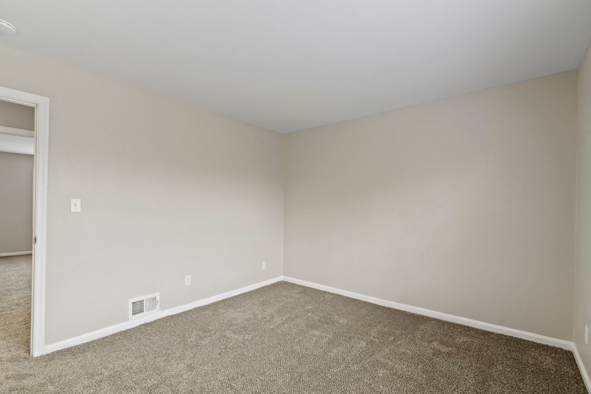 Empty room with tan walls, beige carpet, and an open doorway.