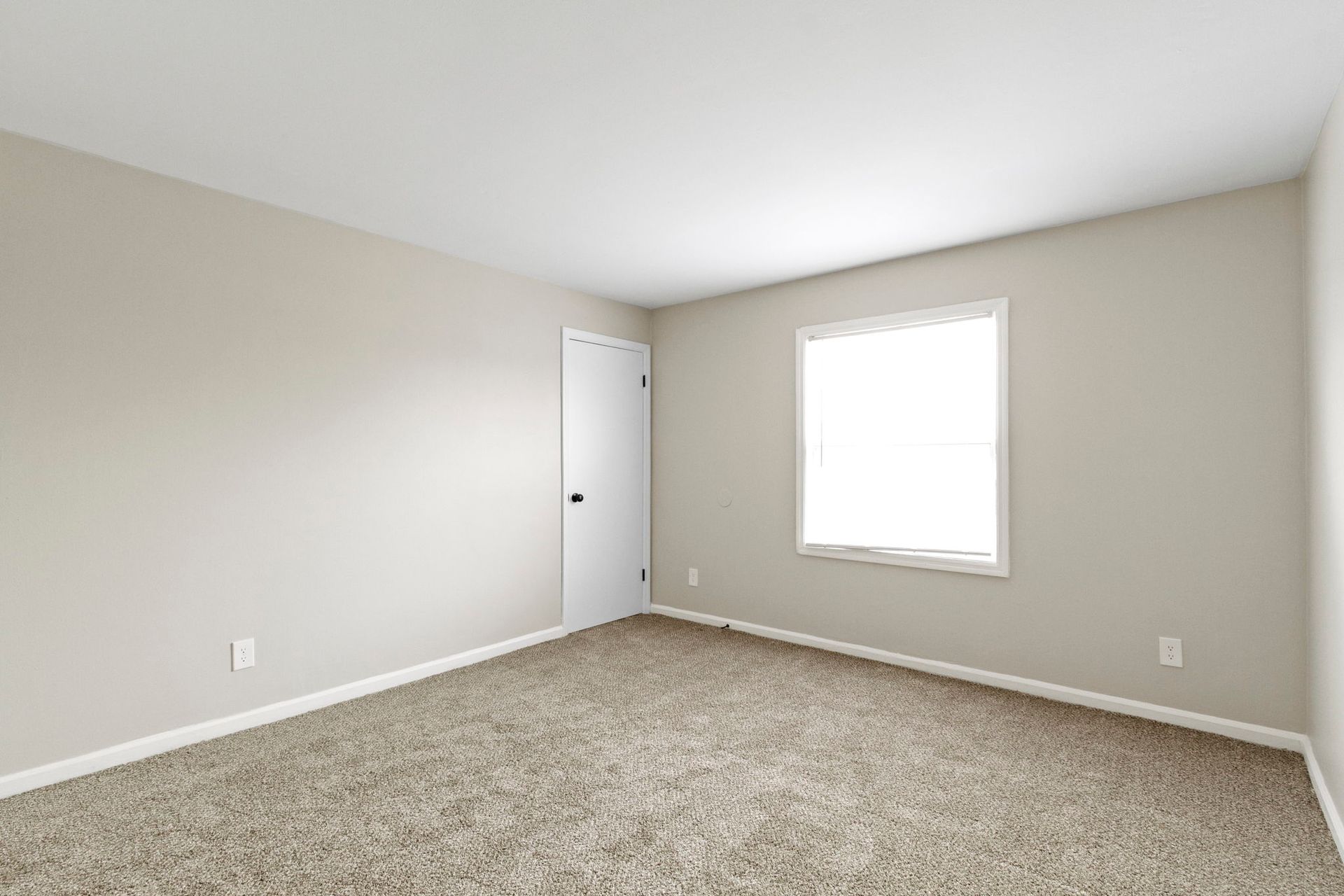 Empty bedroom with tan walls, carpet, and window.