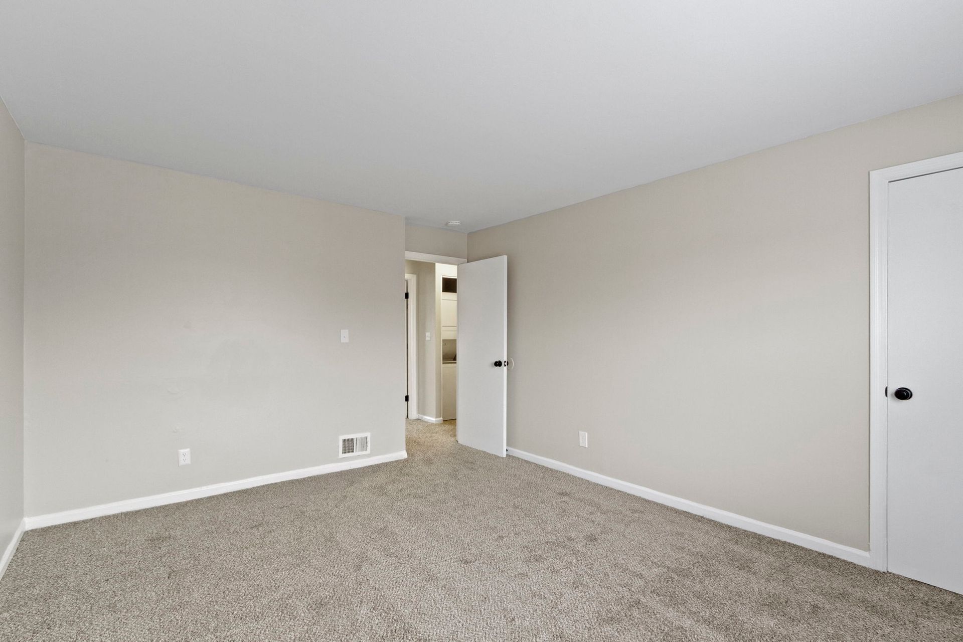 Empty bedroom with beige walls, neutral carpet, and open white door.
