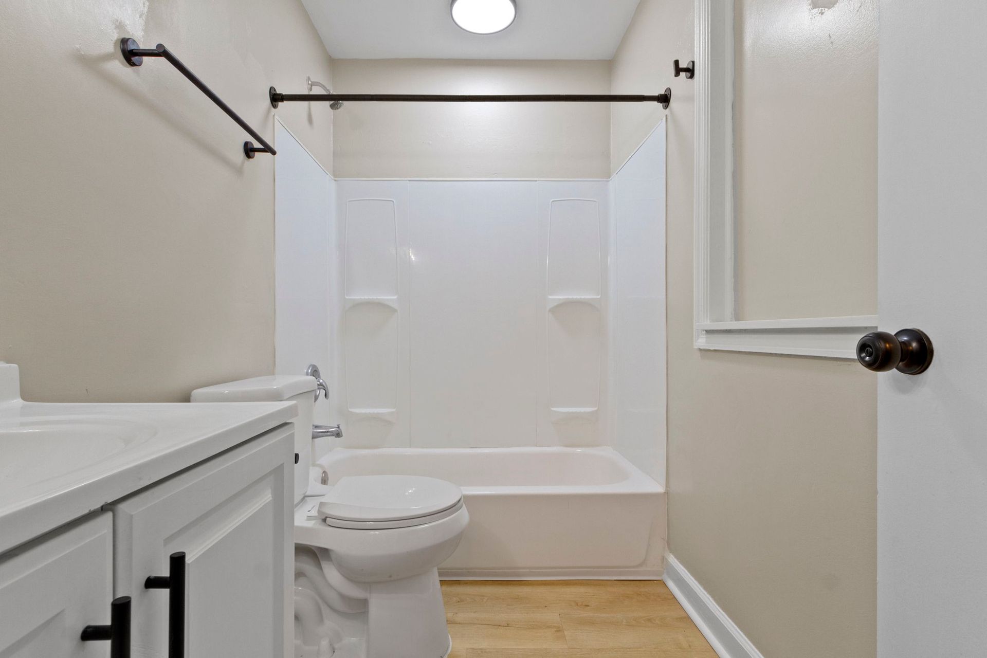 Bathroom with white walls, tub, and vanity. Black hardware and a light-colored floor.
